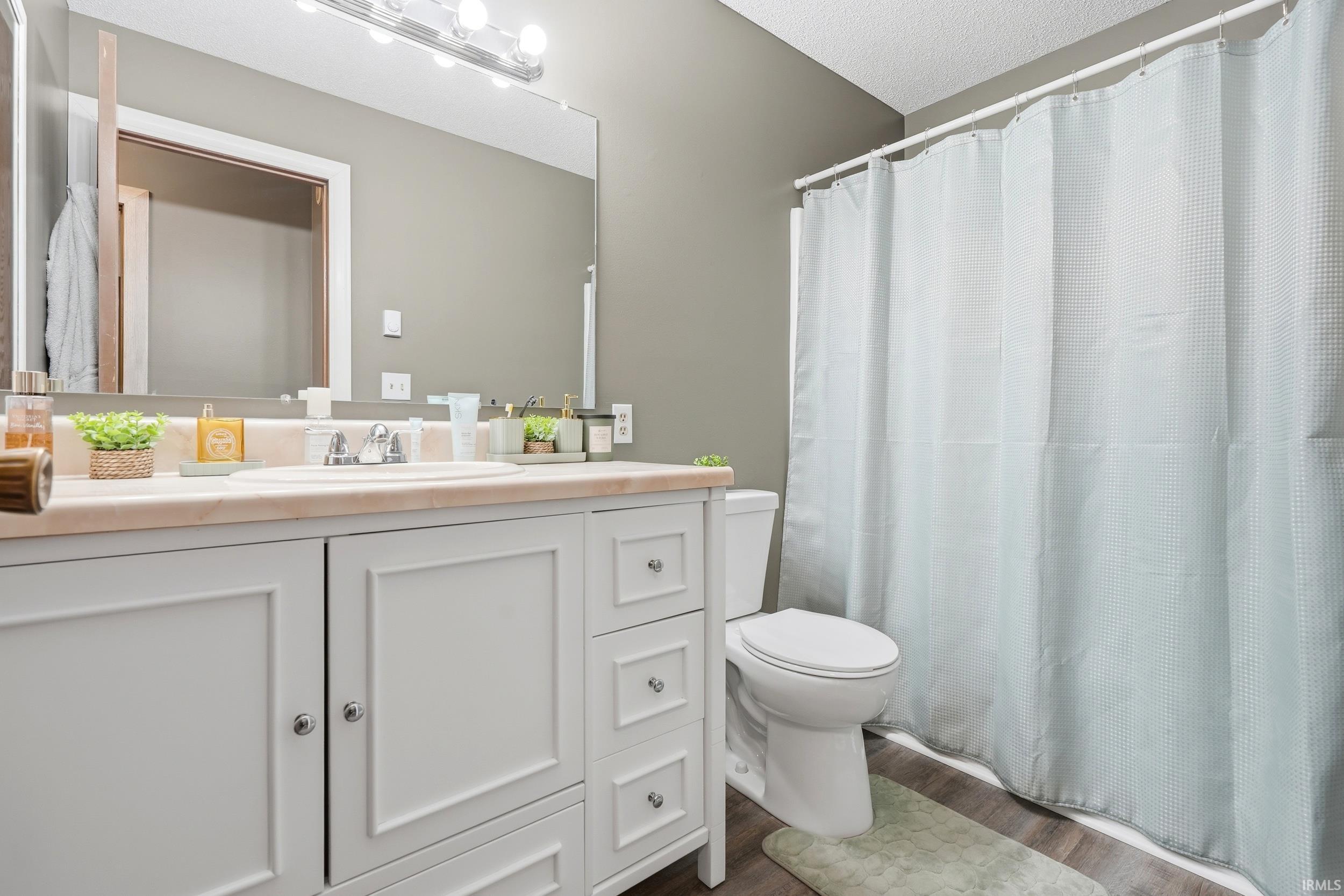 Bathroom featuring a white vanity with paneling and chrome hardware, a light-toned countertop, a rectangular mirror, and a full shower/tub enclosure