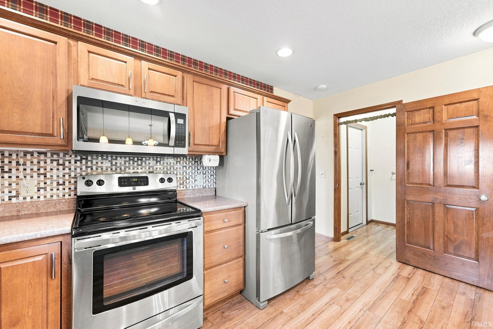 Kitchen featuring wood-finish flooring, stainless steel appliances, wood cabinetry, and a geometric tile backsplash