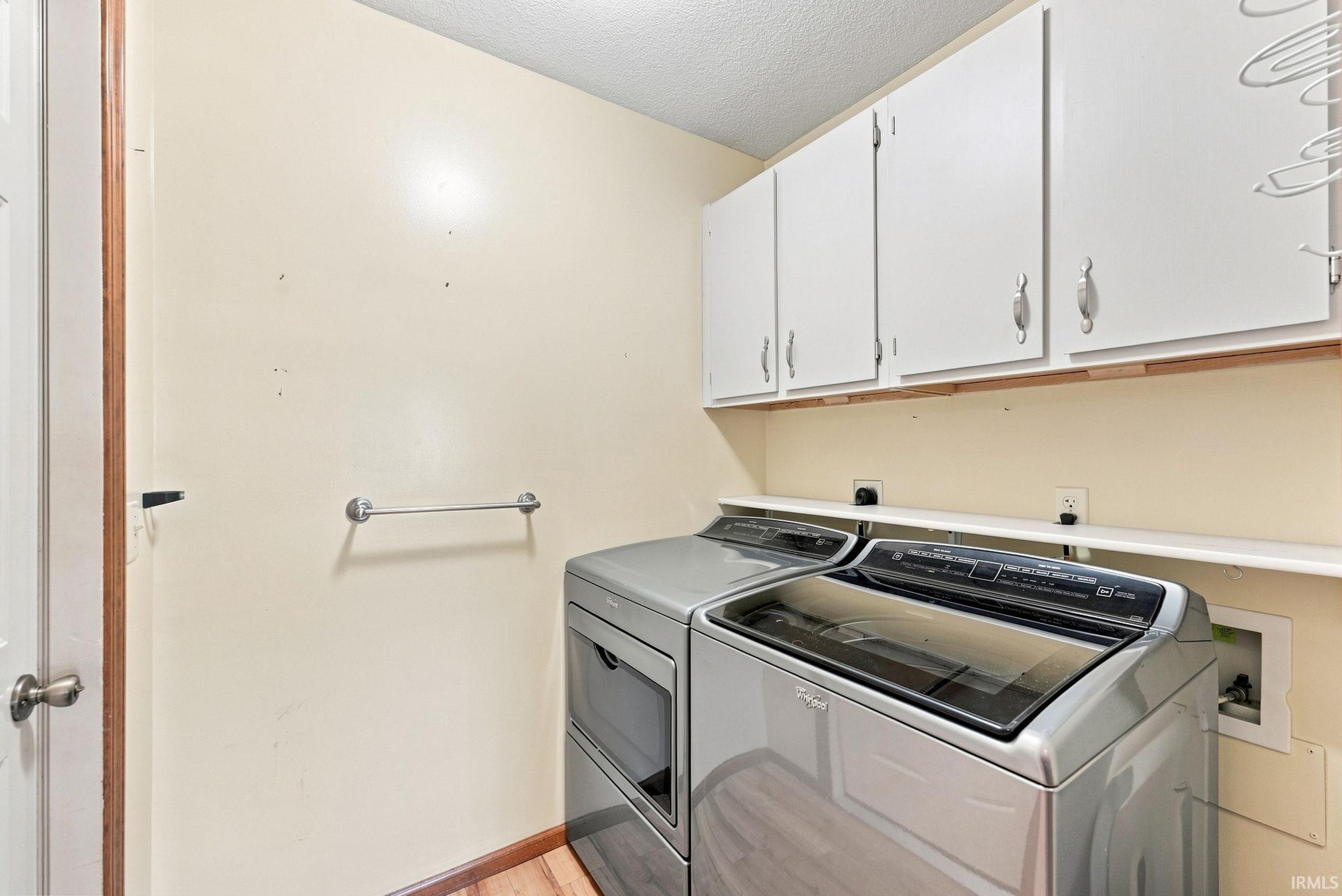 Dedicated laundry space featuring overhead white cabinetry, wood-finish flooring, and a wall-mounted towel bar