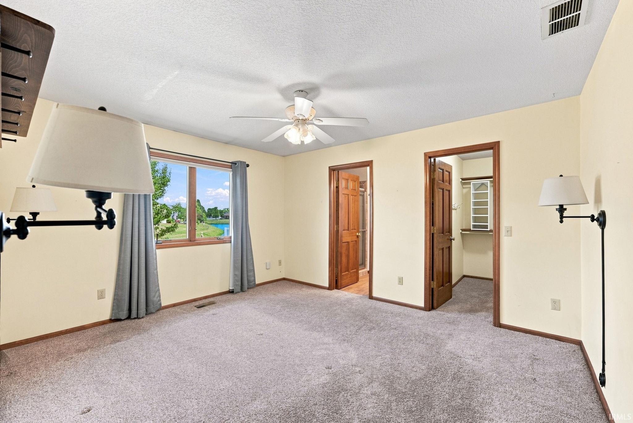 Spacious room featuring a large window with water scenery, two wood-finish doors, a ceiling fan, and grey carpet