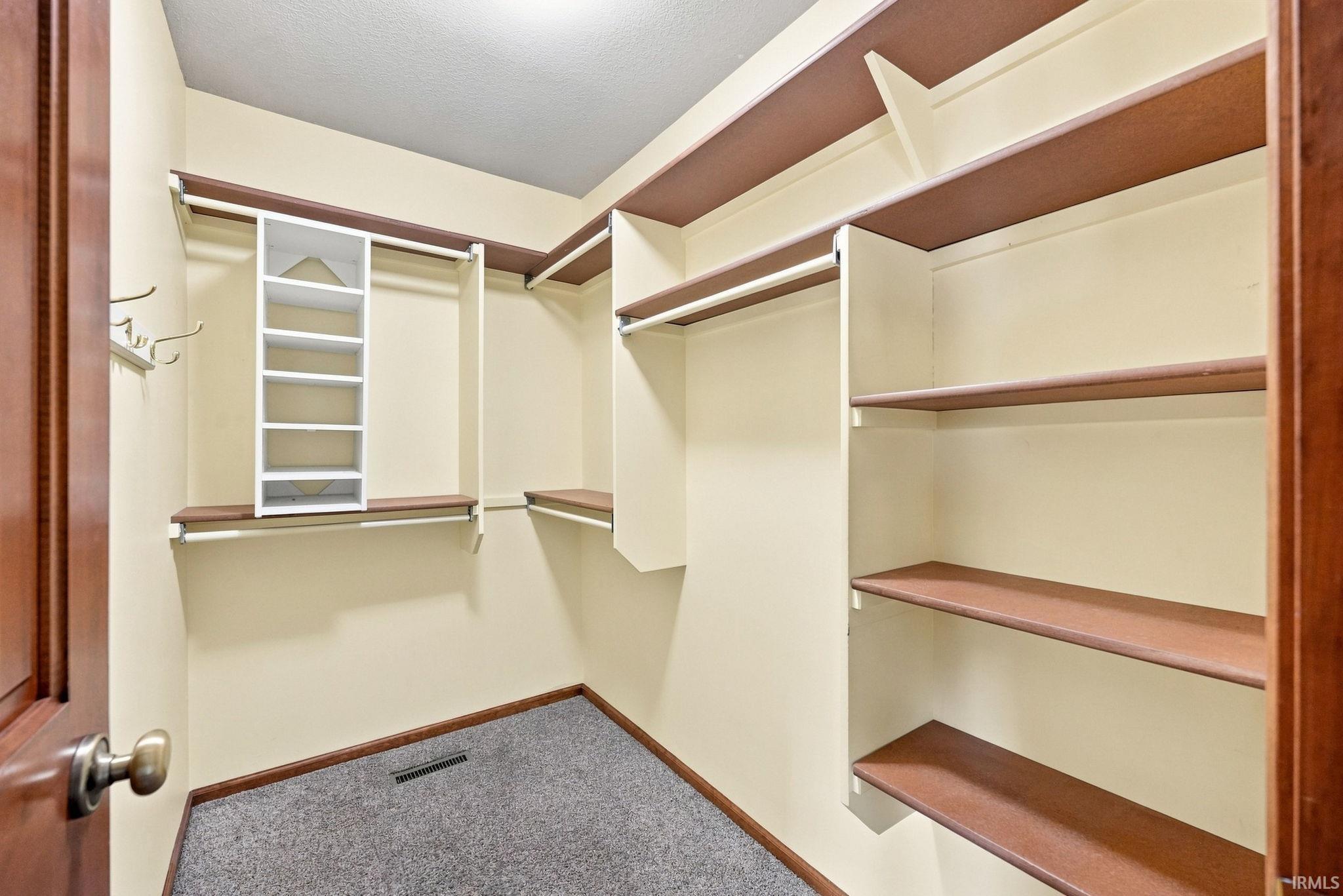 Spacious walk-in closet featuring extensive built-in shelving, multiple hanging rods, corner shelving units, and a central shelving tower