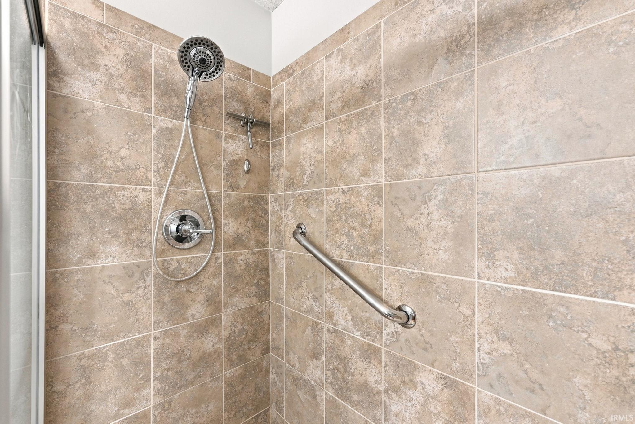 Tiled shower enclosure featuring a handheld showerhead, polished chrome fixtures, and a glass panel enclosure