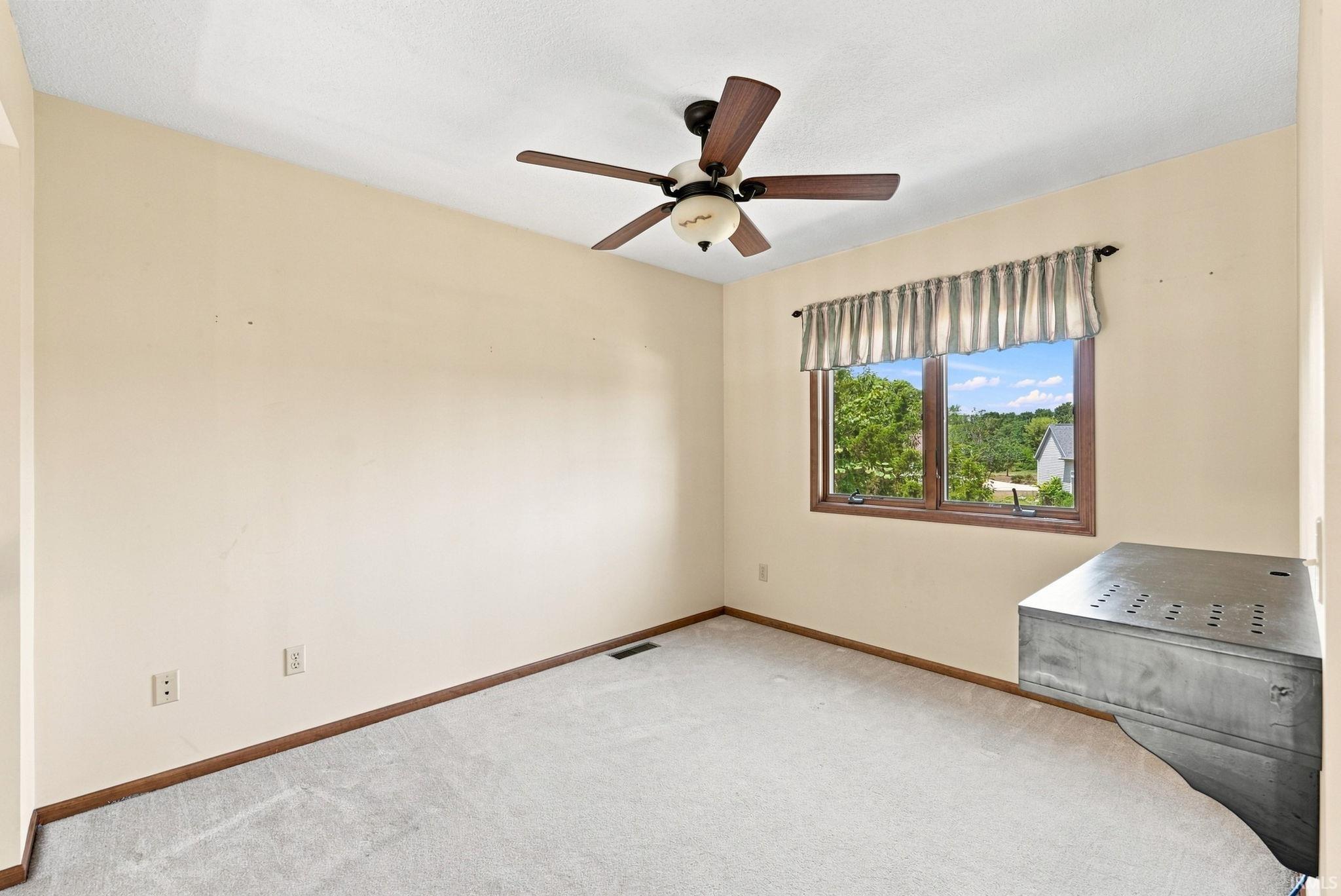 Carpeted room with a ceiling fan, a window with wood-finish trim, and a built-in wall unit
