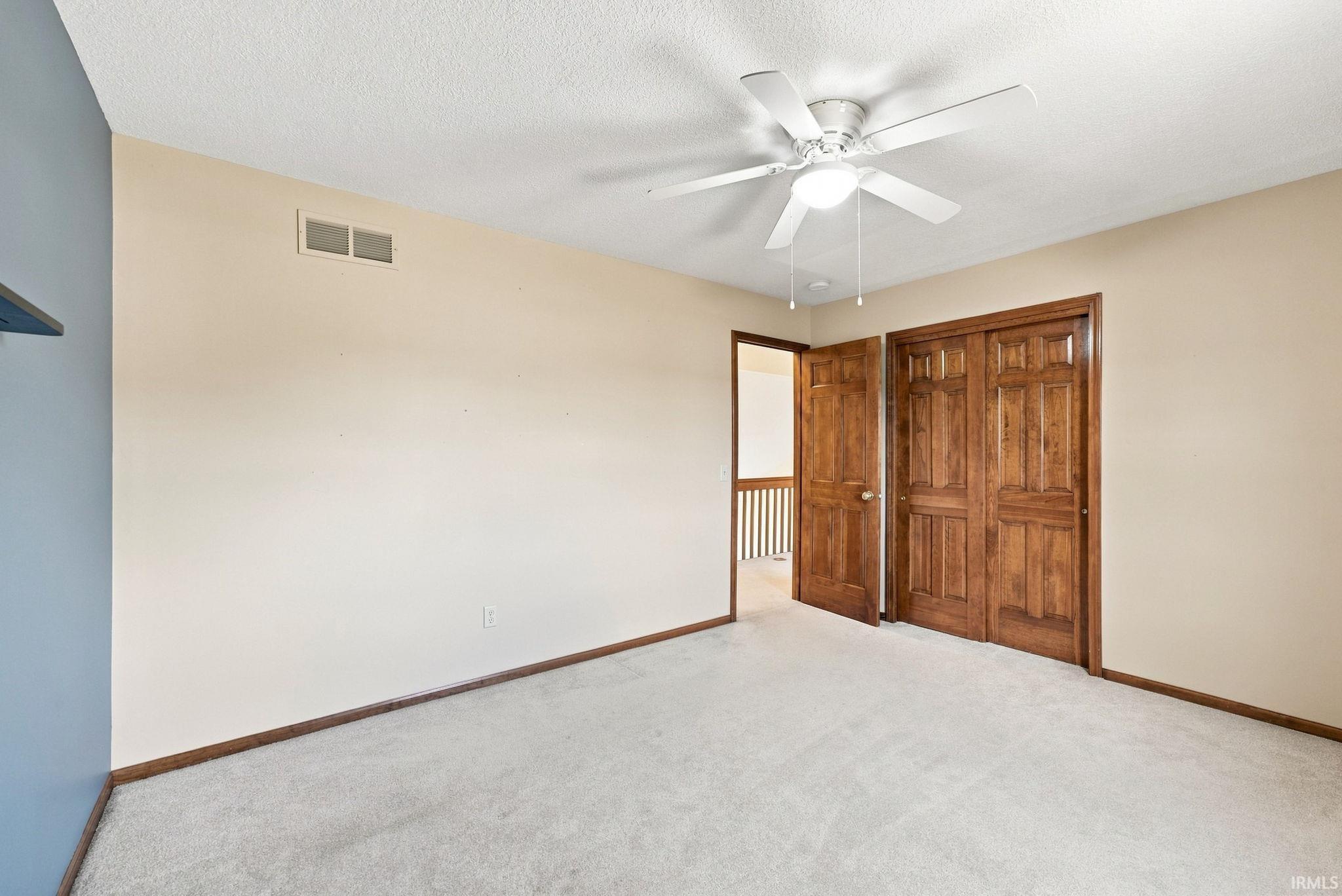 Carpeted room featuring a ceiling fan with integrated lighting, wood-finish bi-fold closet doors, and wood-finish trim