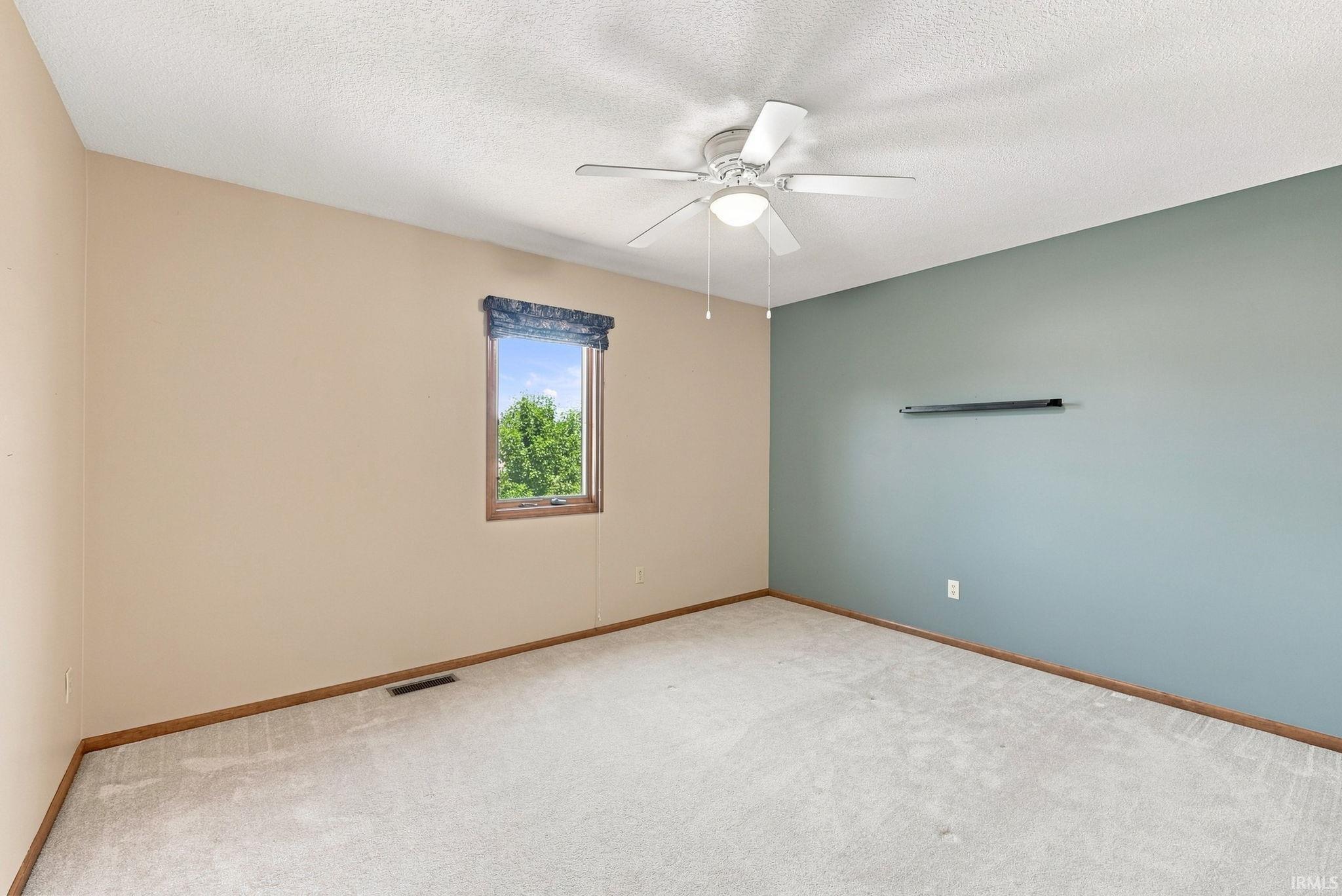 Spacious room featuring carpeted flooring, a ceiling fan with integrated lighting, and a single window with a valance