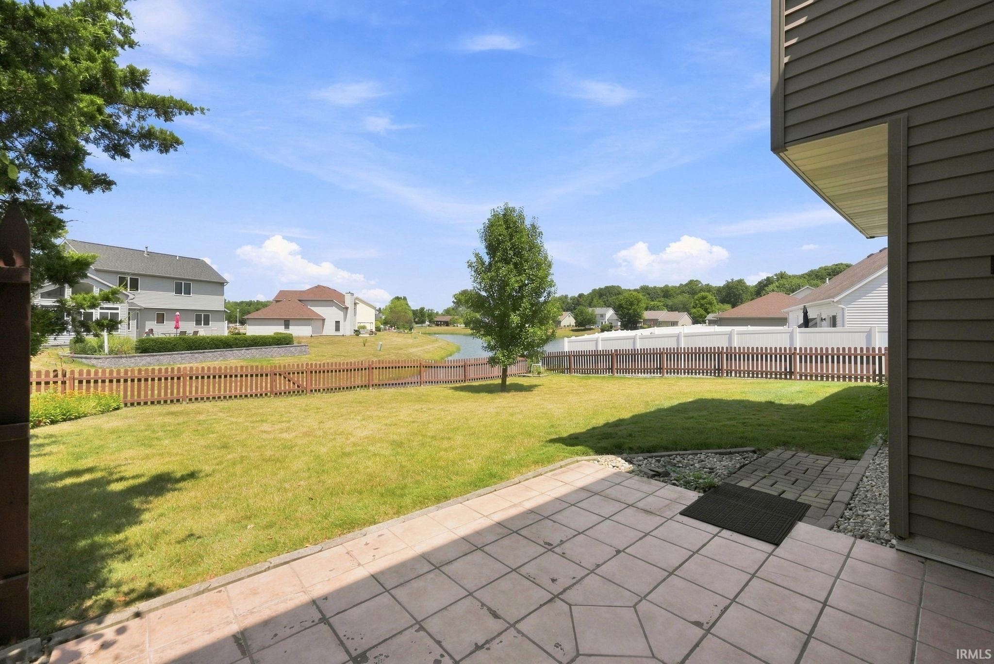 Expansive backyard featuring a large paved patio, green lawn, and a light wood picket fence