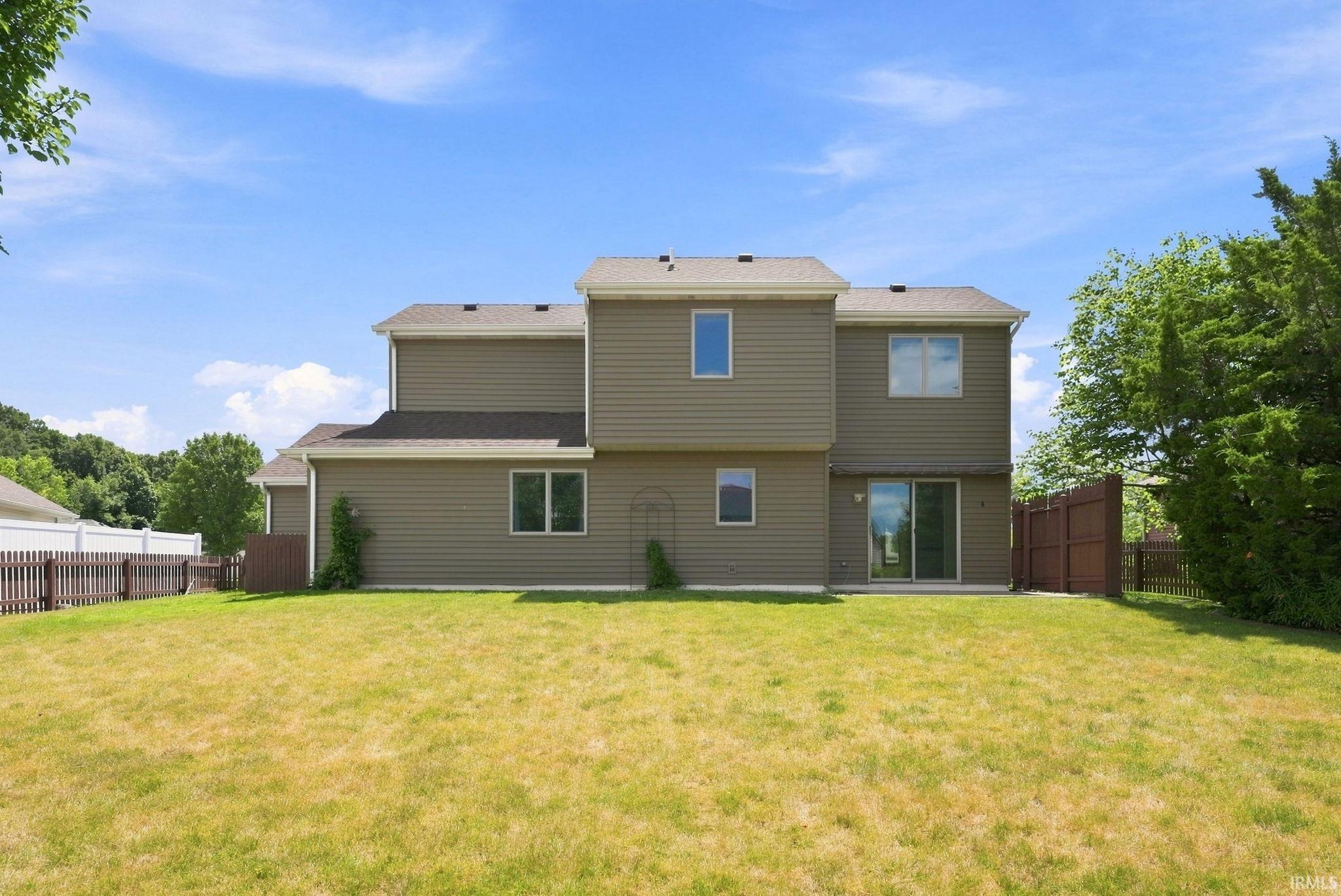 Expansive backyard featuring a large green space, mature trees, a privacy fence, and a patio area with sliding glass door access to the residence