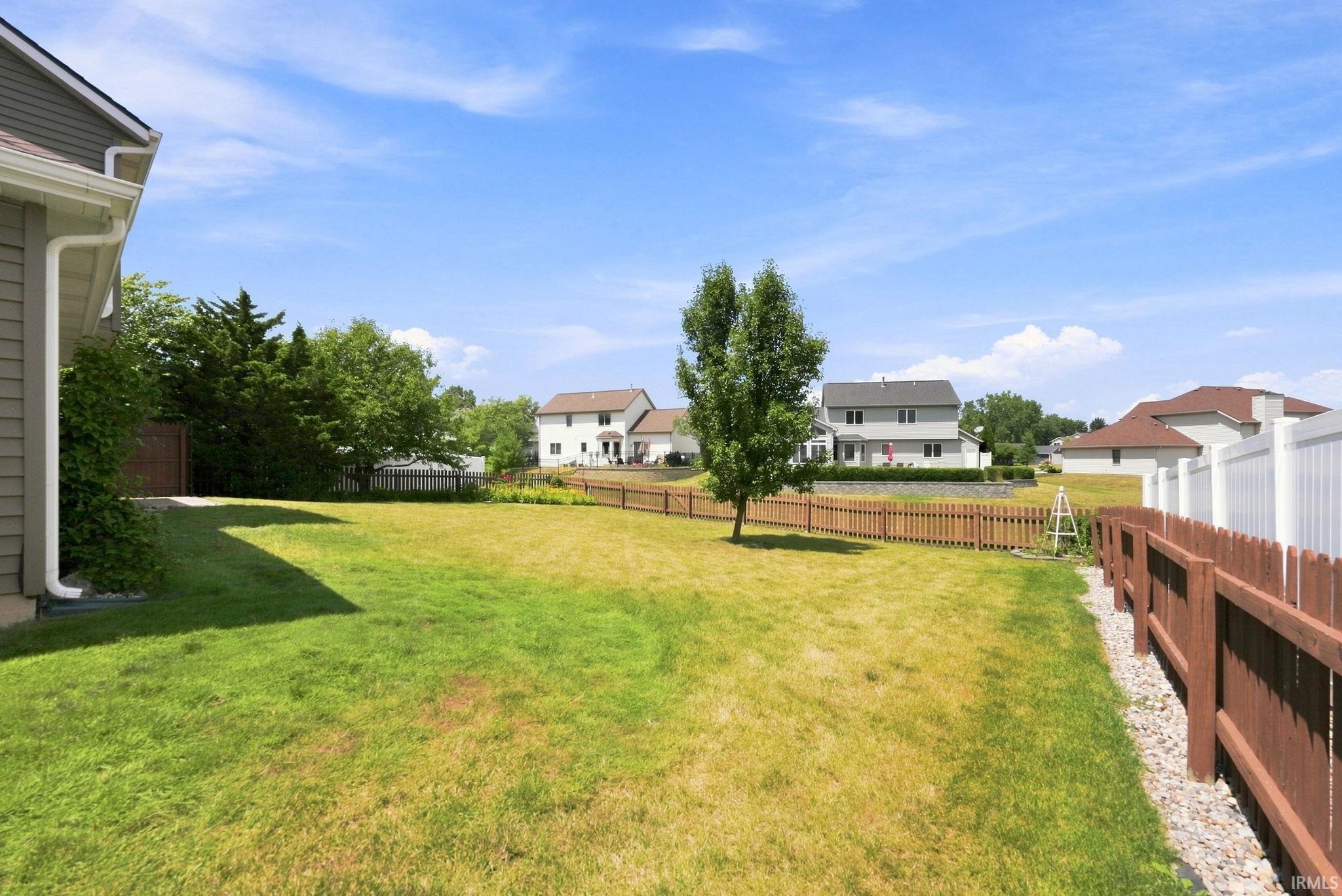 Expansive backyard featuring a mature tree, brown picket fencing, and white privacy fencing