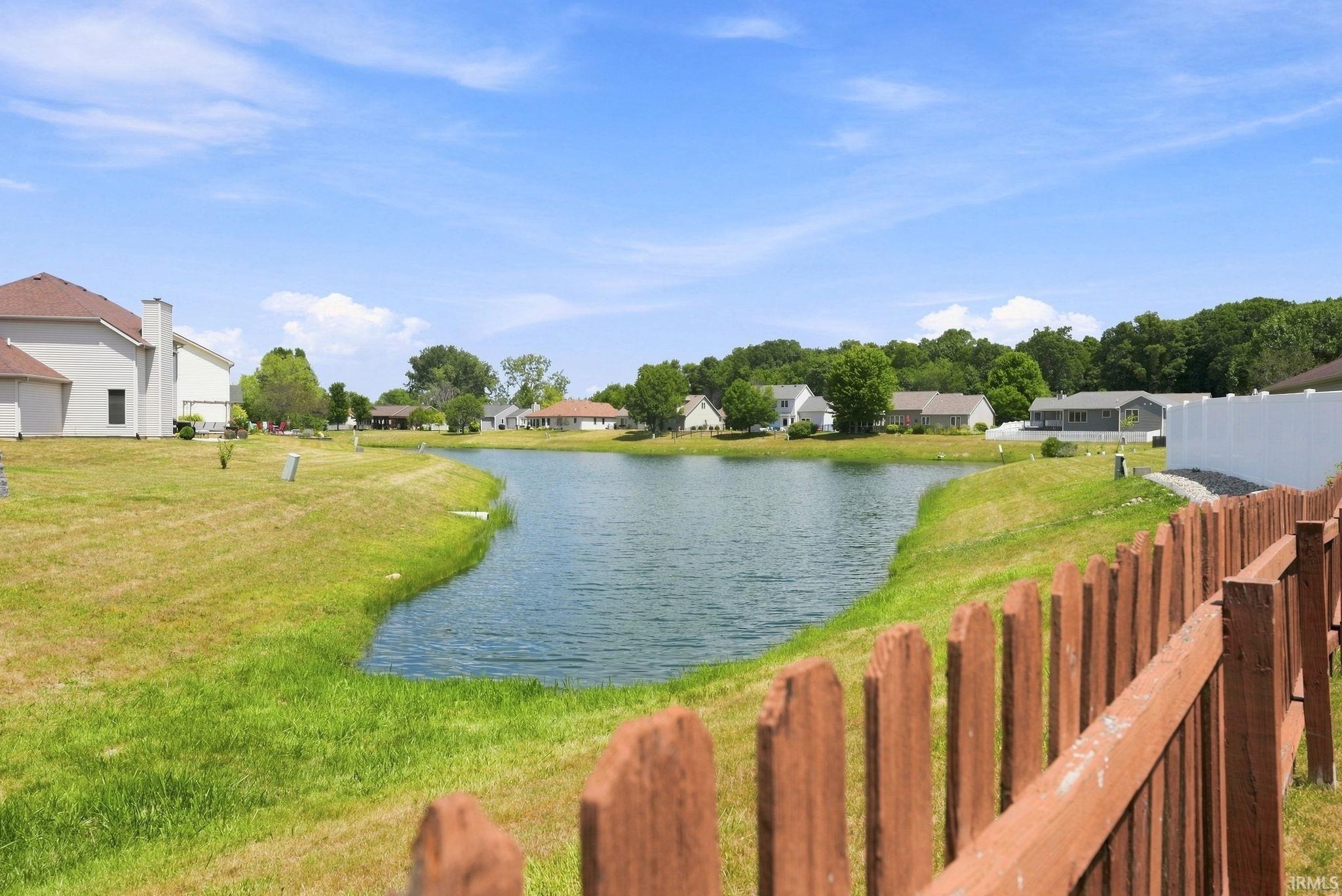Expansive backyard with a serene pond, natural landscaping, and a partial wooden fence