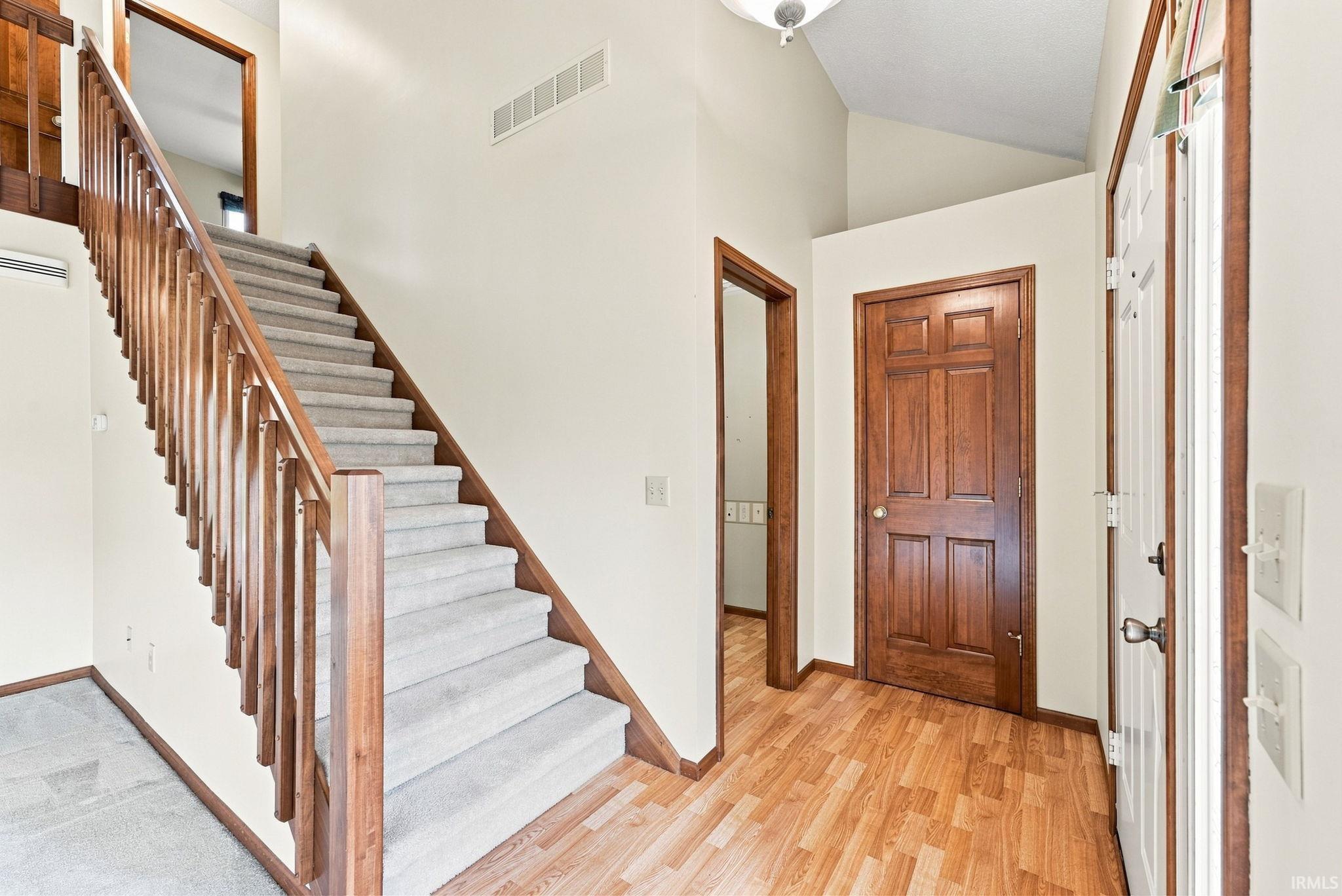 Welcoming foyer showcasing a grand wooden staircase with turned balusters and a polished wood-finish handrail, complemented by warm wood-finish flooring throughout