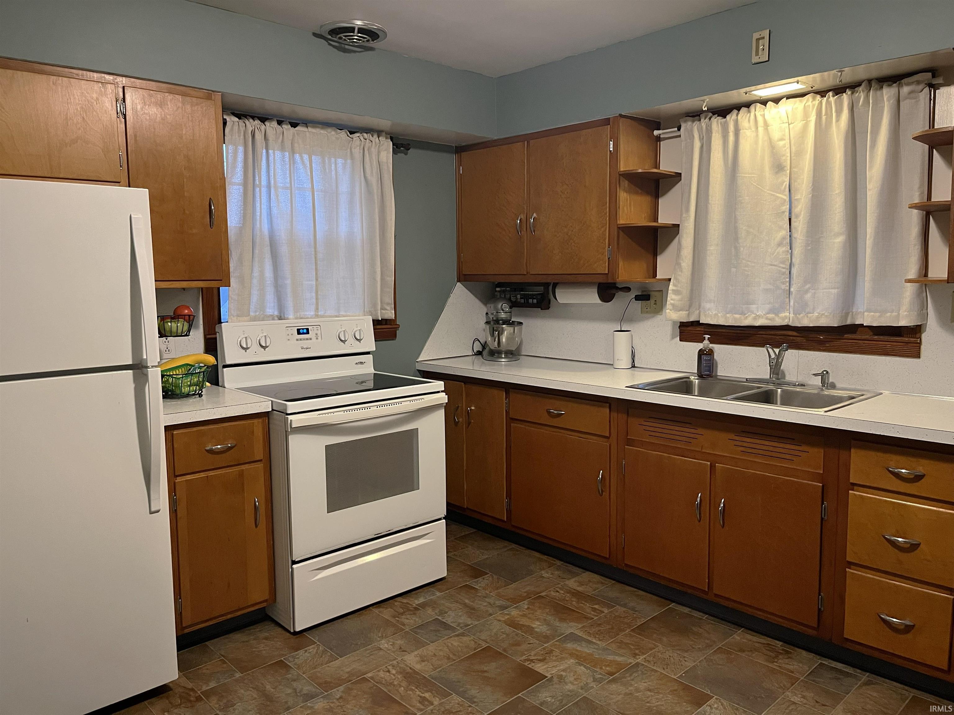 Kitchen featuring wood-finish cabinetry with silver hardware, light-toned countertops, and a double basin stainless steel sink