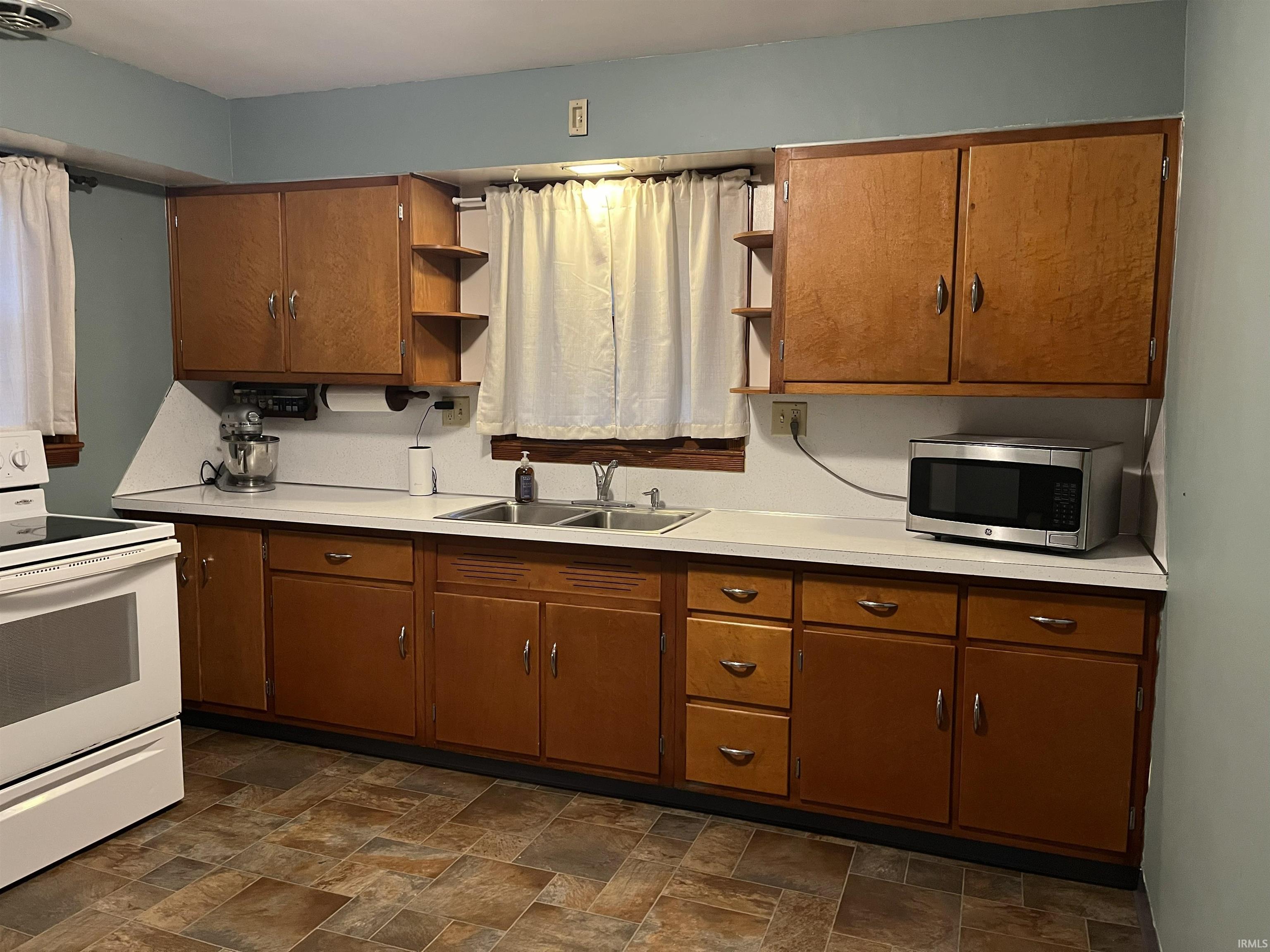 Kitchen featuring wood cabinetry with ample storage, white countertops, and a double basin stainless steel sink