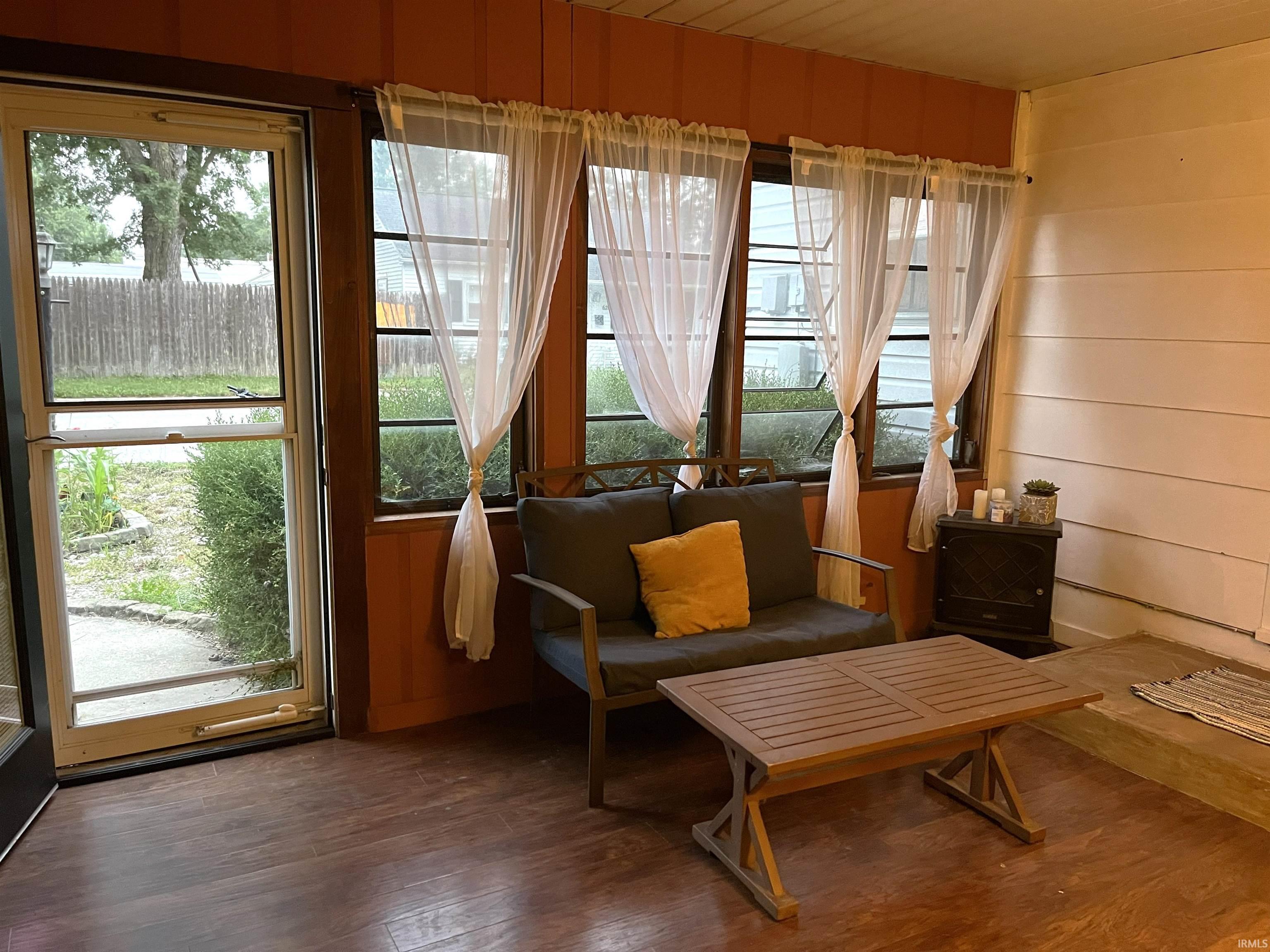 Inviting enclosed porch with wood-finish flooring, multiple windows, and a full-light storm door