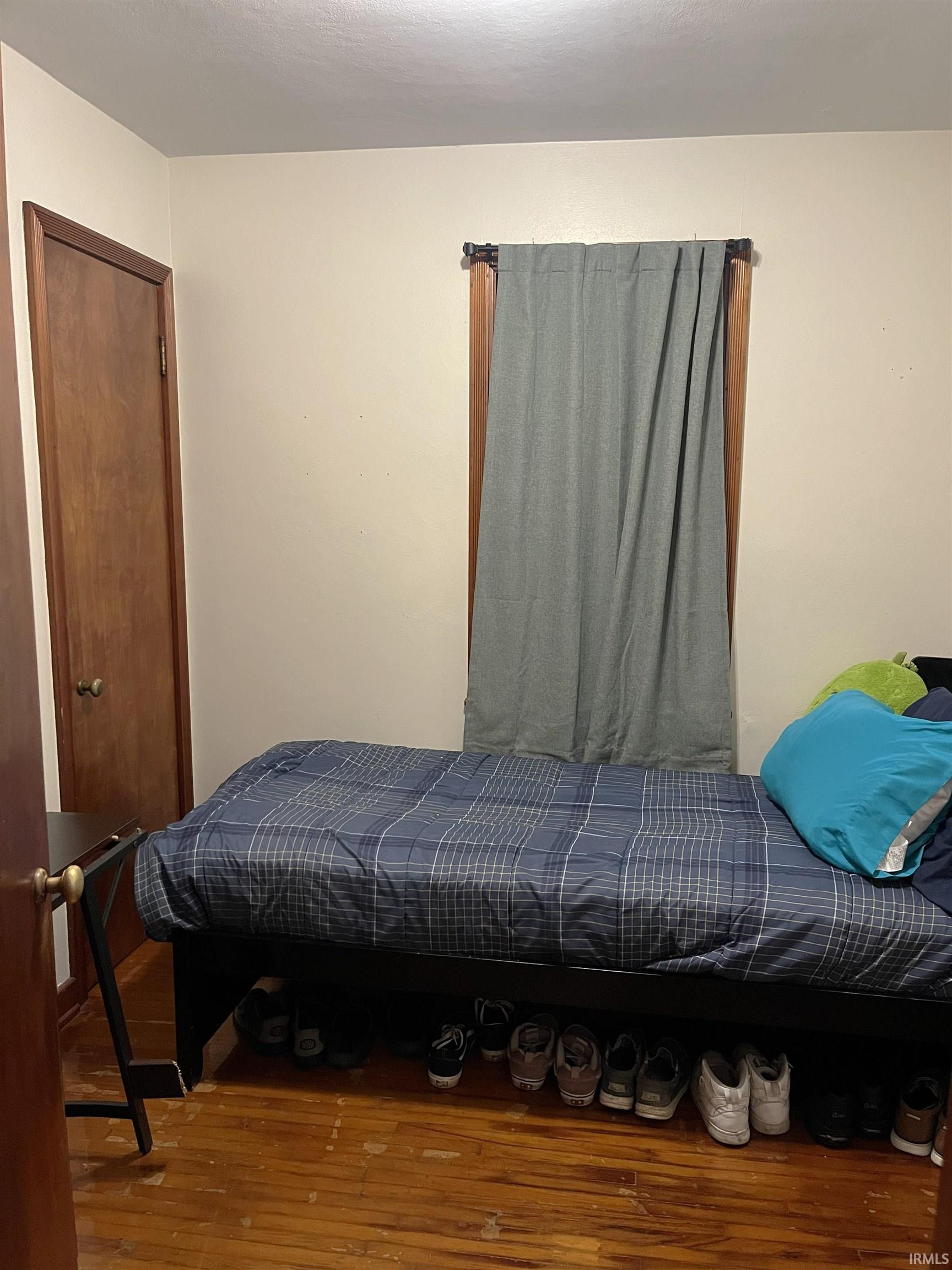 Bedroom featuring wood-finish flooring, light-toned walls, and a window with wood trim
