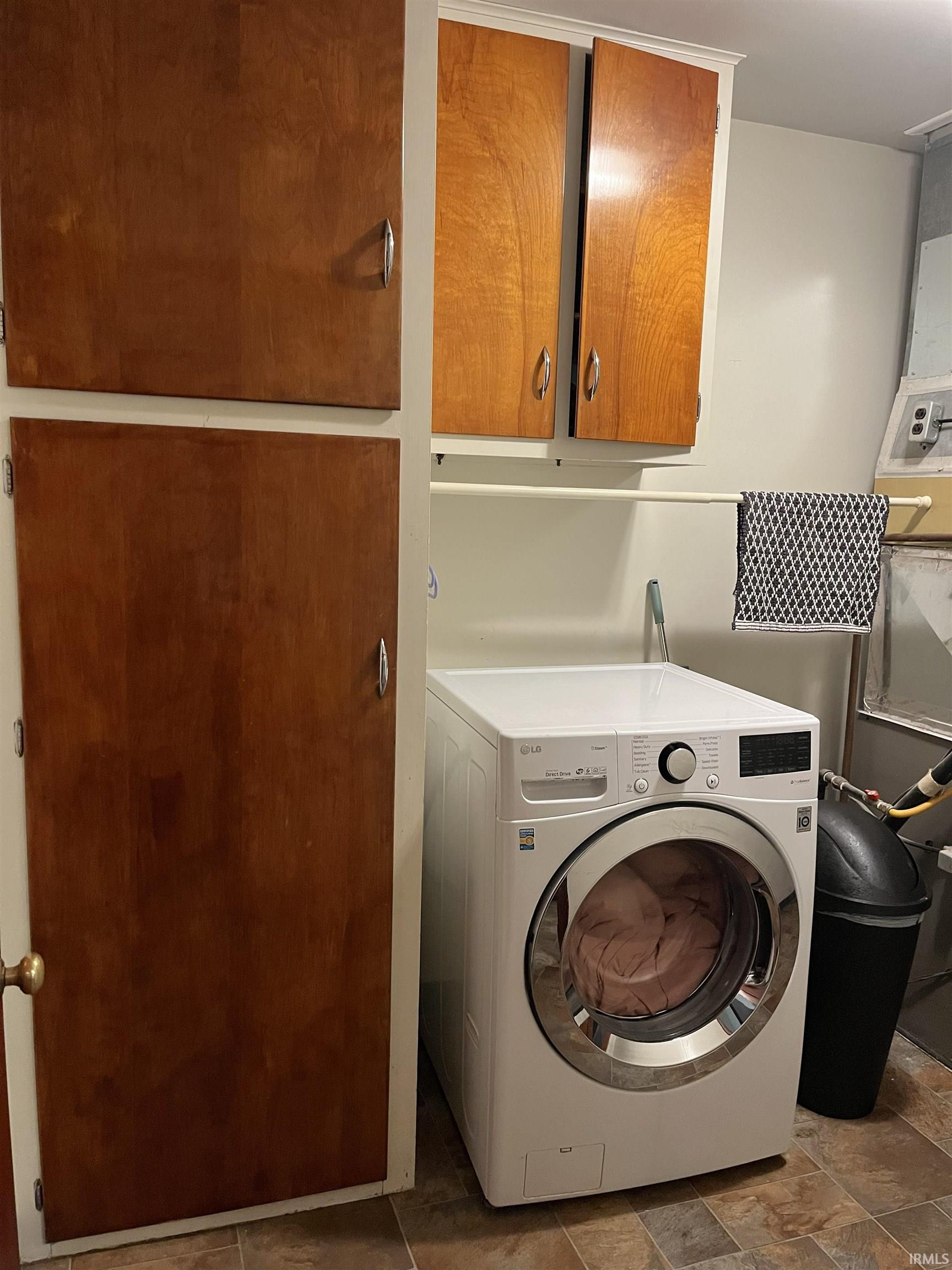 Dedicated laundry area featuring a front-loading washing machine, wood-finish cabinetry, and tiled flooring