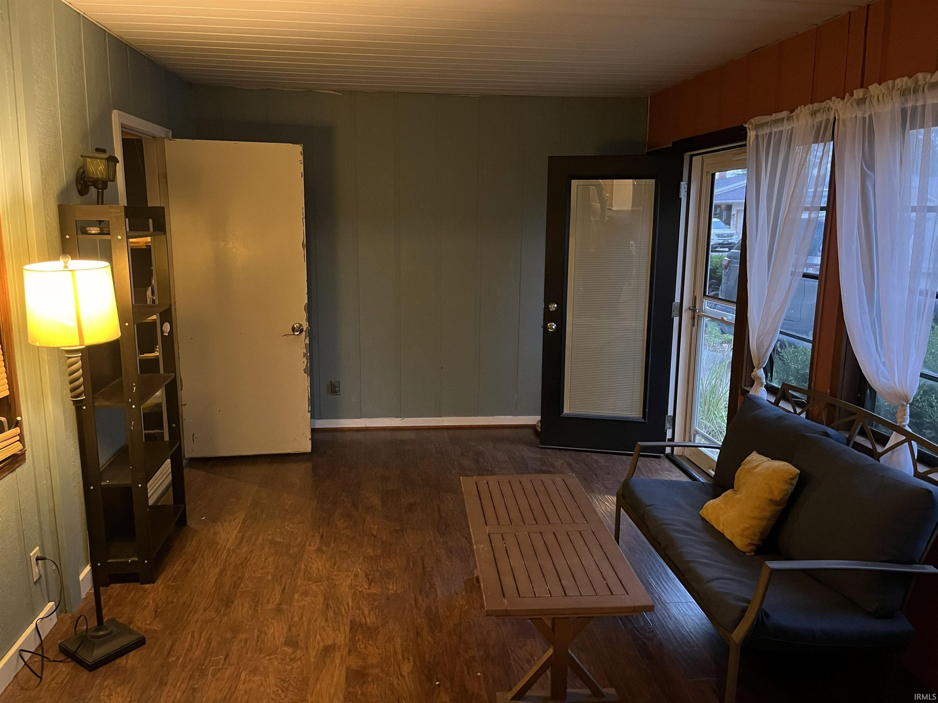 Room featuring wood-finish flooring, two doors, and a window with sheer curtains