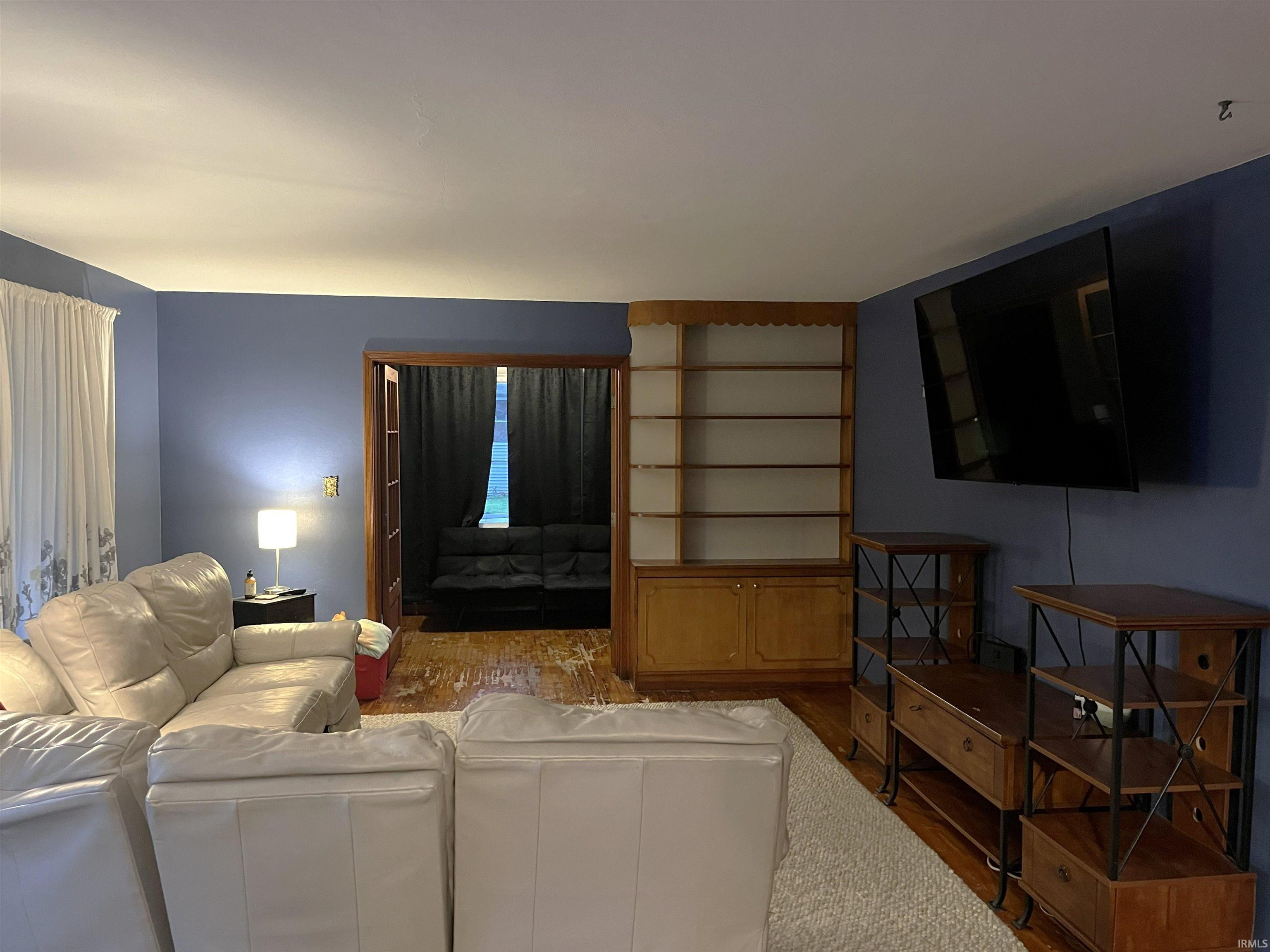 Living area featuring a built-in wooden bookcase with shelving and lower cabinetry, wood-finish flooring, and a doorway opening to an additional room