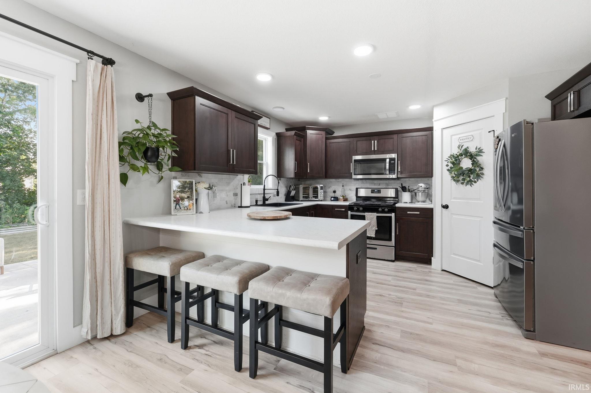Well-appointed kitchen featuring dark wood cabinetry, stainless steel appliances, and light-toned wood-finish flooring