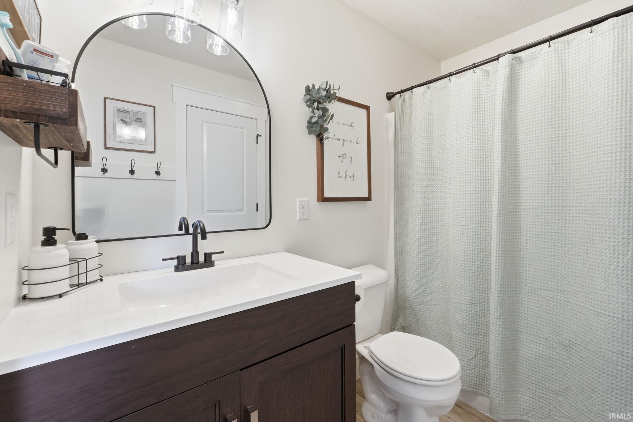 Bathroom featuring a dark wood-finish vanity with a white countertop and integrated sink, matte black faucet, and an arched mirror