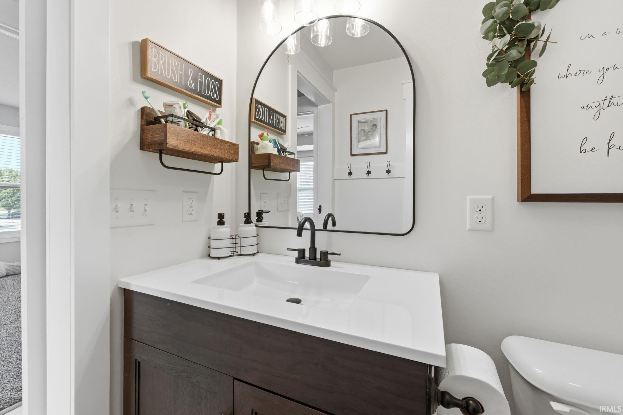 Bathroom vanity with a white countertop and integrated sink, a dark wood-finish cabinet, and a black-framed arched mirror