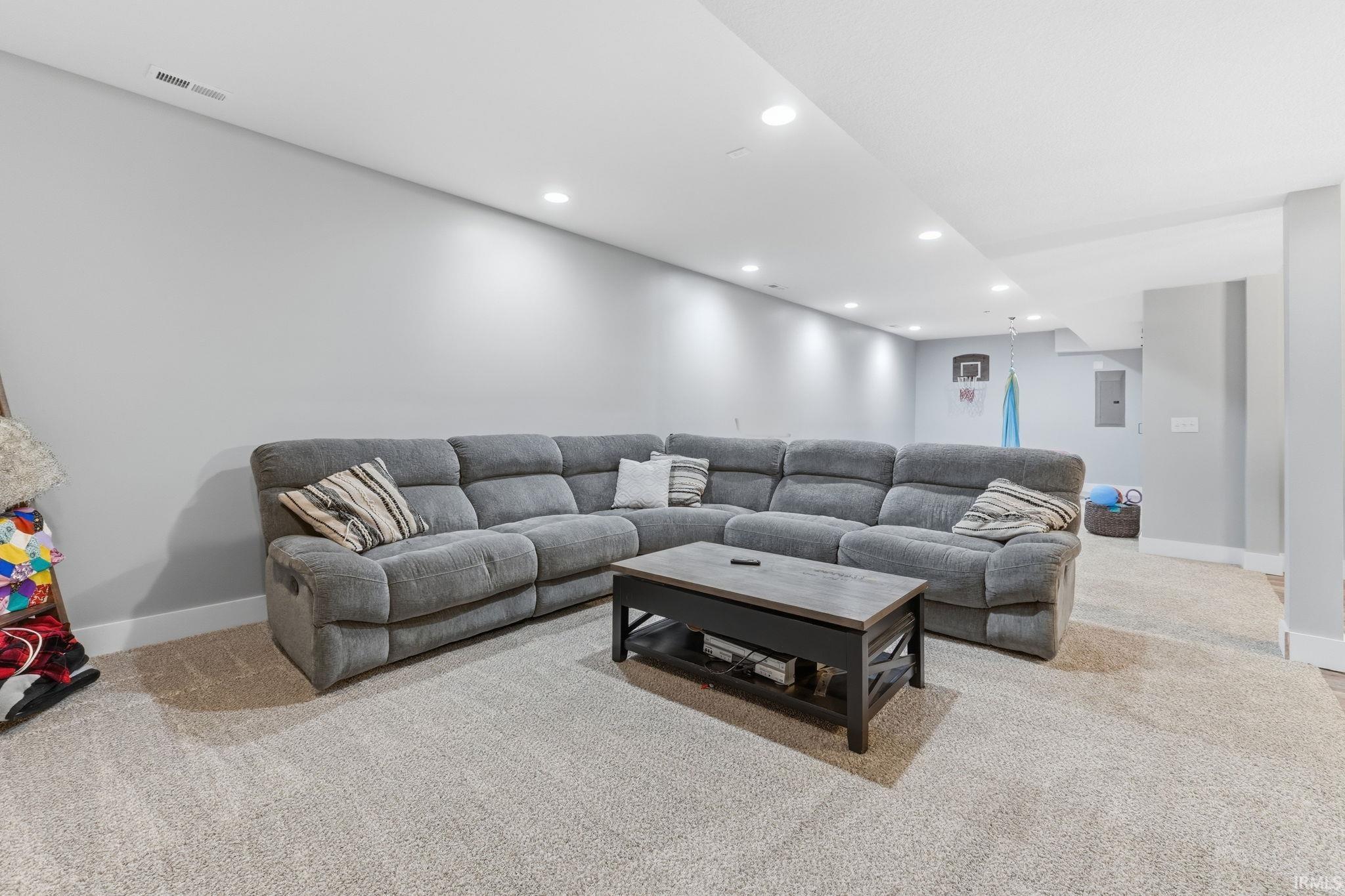 Spacious lower-level room featuring light gray walls, plush carpet flooring, recessed lighting, and white baseboards