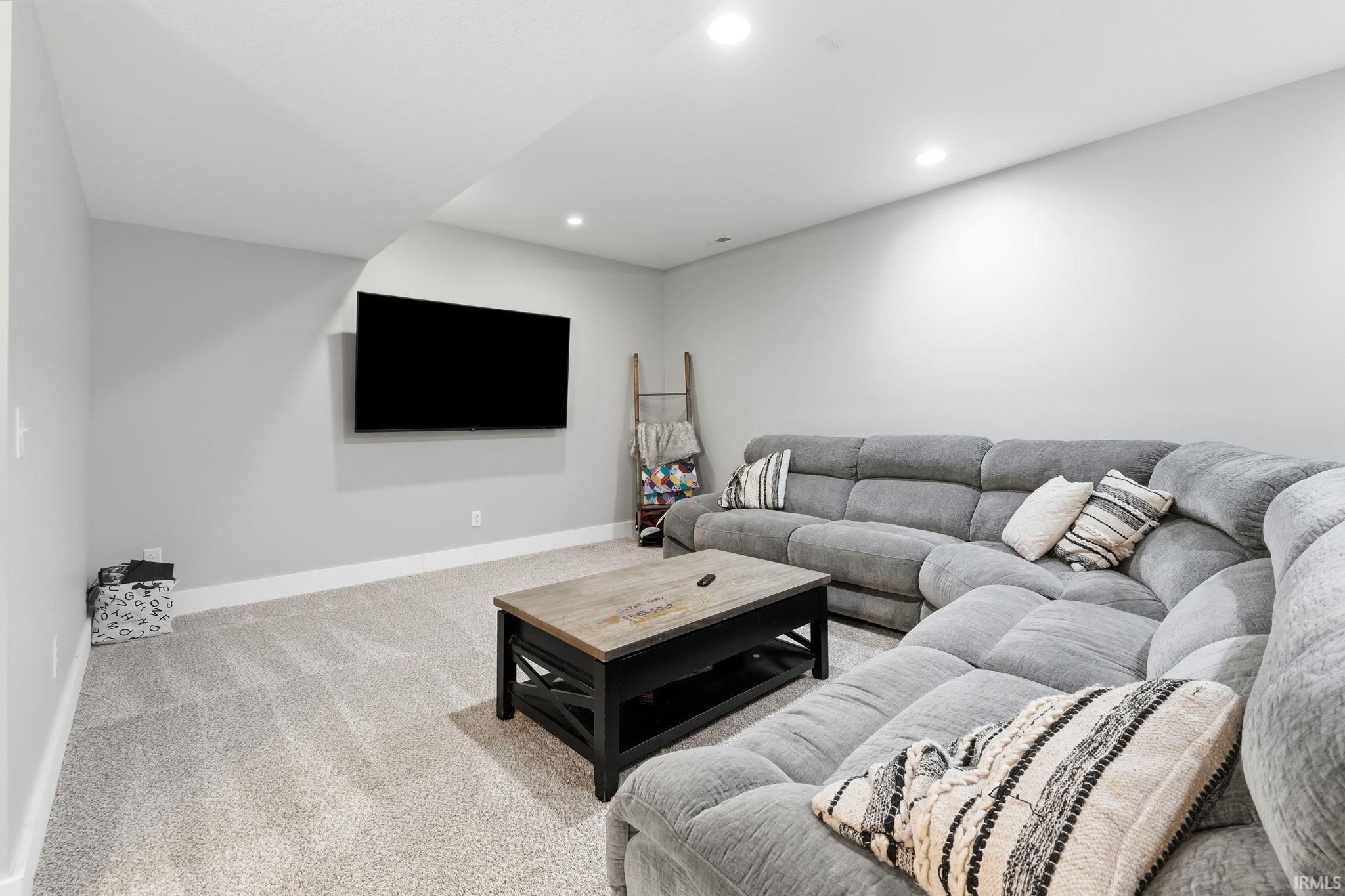 Recessed lighting illuminates this room featuring light gray carpeting and white baseboards