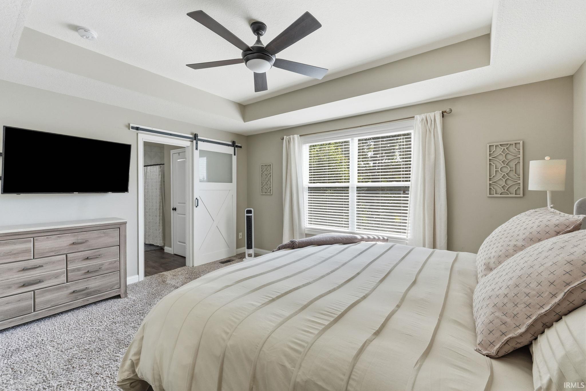 Spacious room featuring a tray ceiling with a ceiling fan, a large window with blinds, and soft gray carpeting