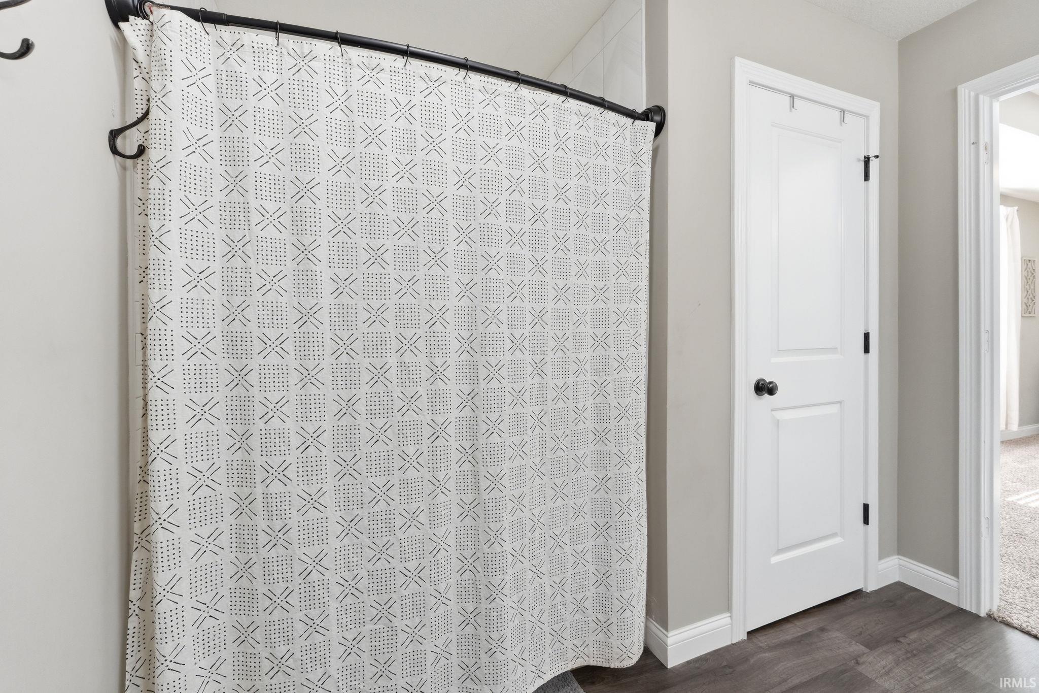 Bathroom featuring a shower with a curved rod, white paneled door with black hardware, wood-finish flooring, and light gray wall paint