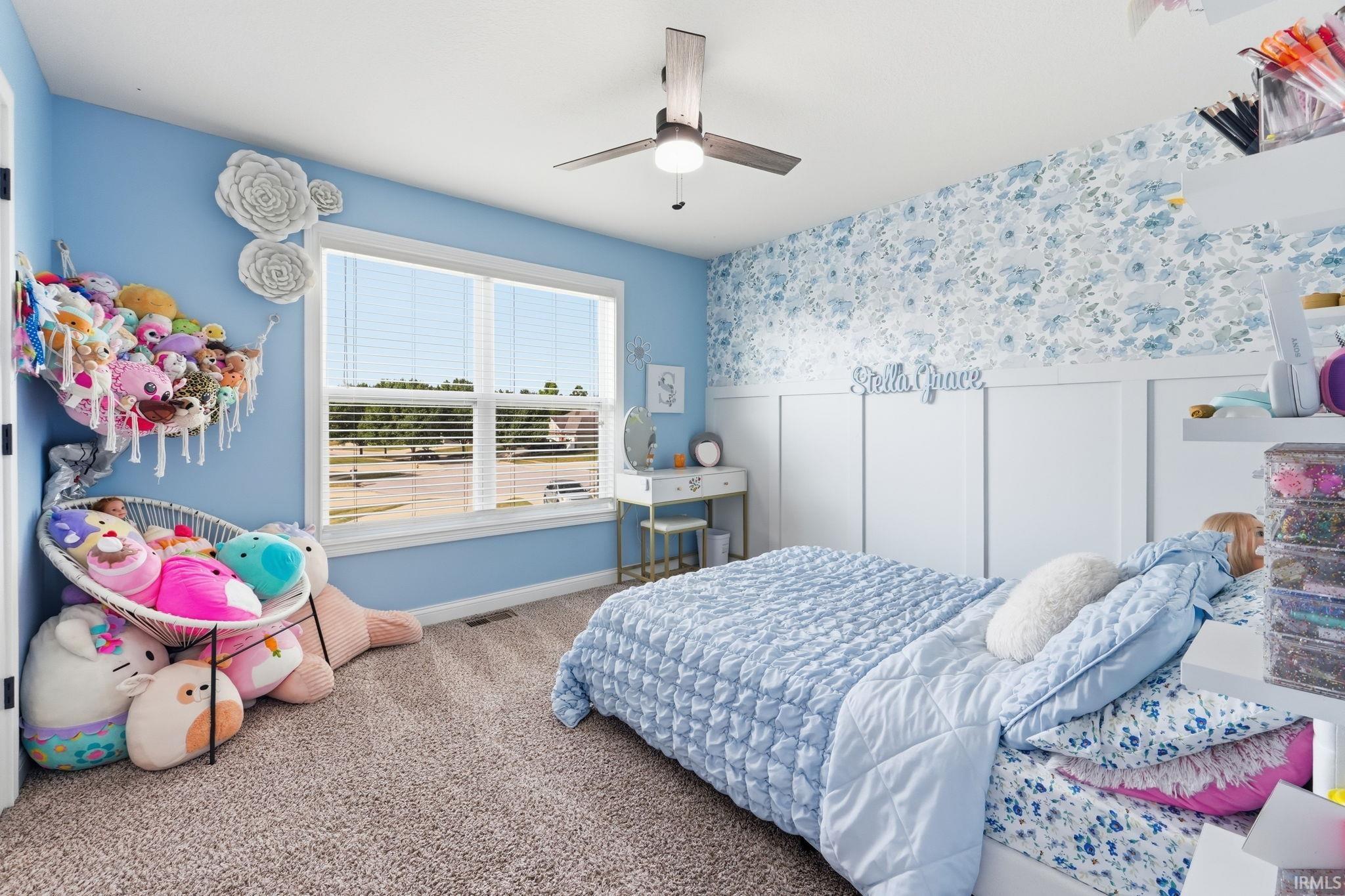 Light blue painted walls featuring a large window with horizontal blinds, a decorative floral accent wall with white wainscoting, and a ceiling fan with integrated lighting