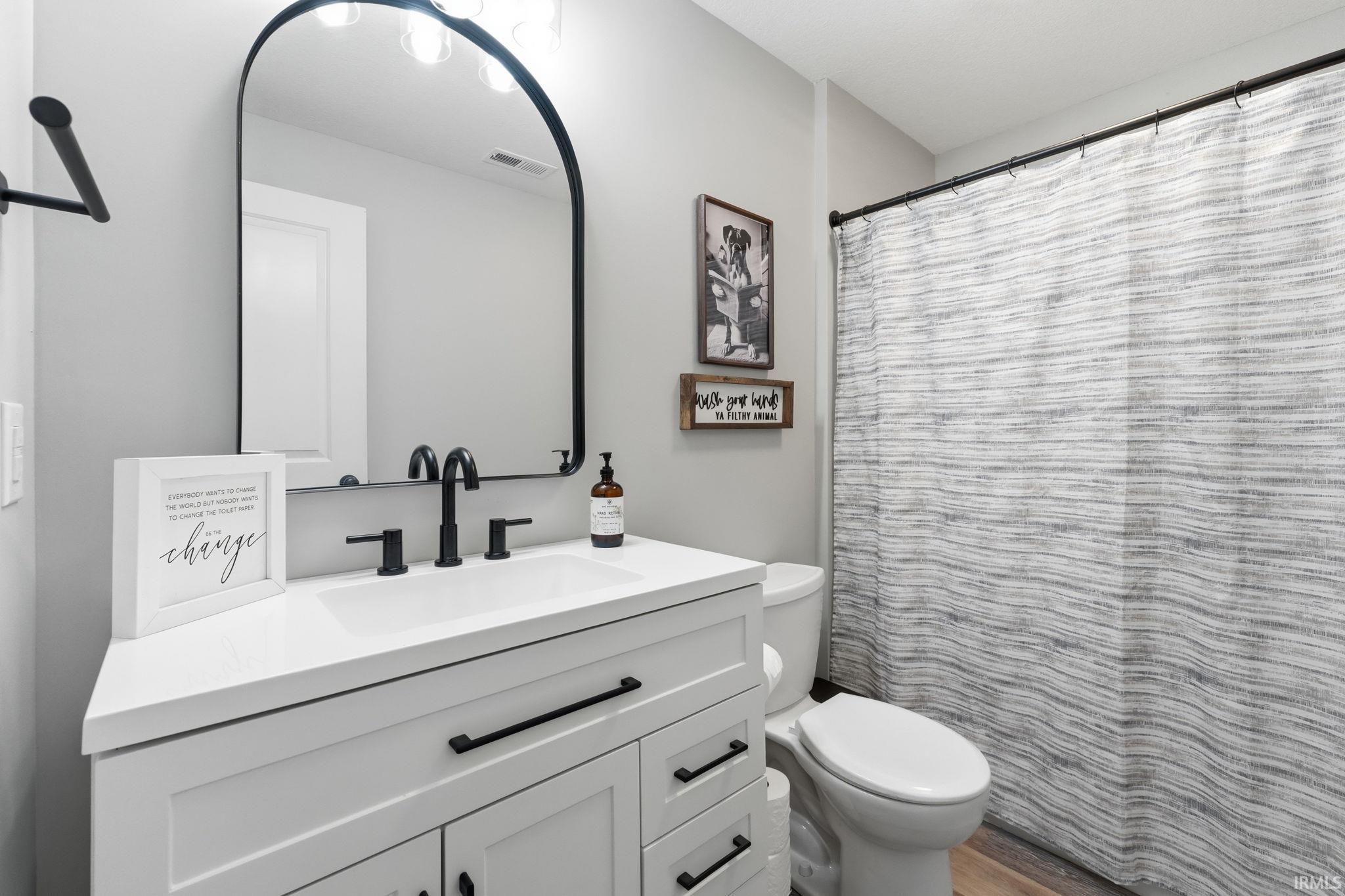 Bathroom featuring a white vanity with integrated sink, matte black faucet, and an arched black-framed mirror with globe lighting