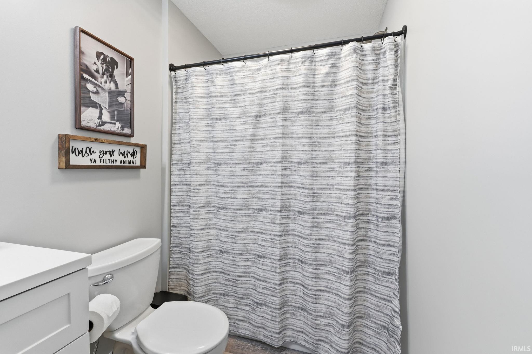 Bathroom featuring a white toilet, light gray wall paint, and a shower curtain on a dark rod
