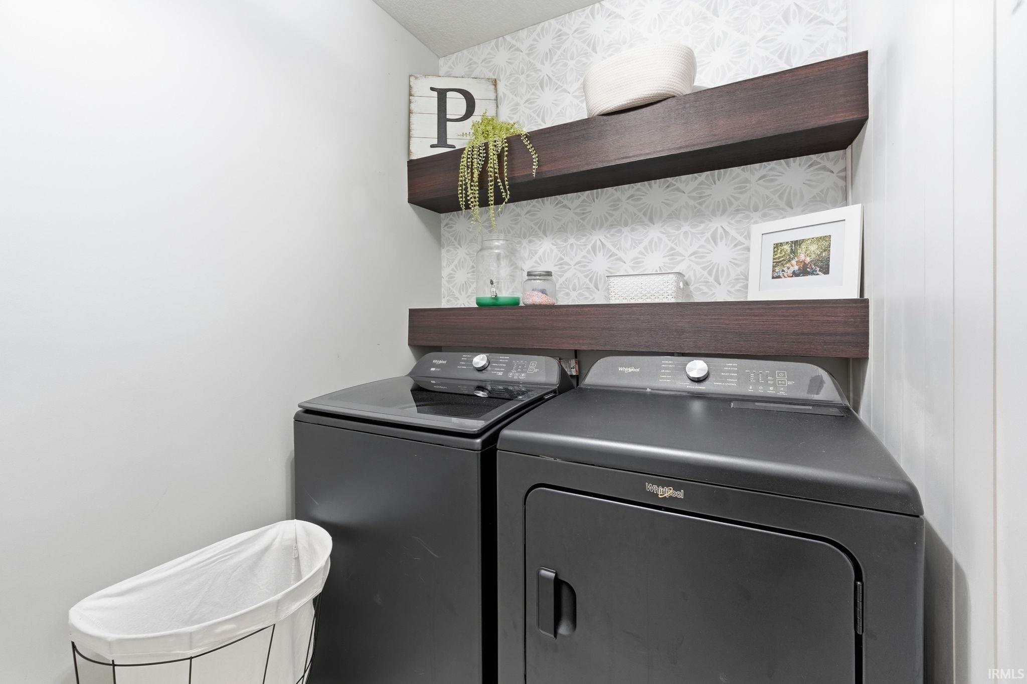 Laundry area featuring a black washer and dryer set, two dark wood-finish floating shelves, and accent wallpaper