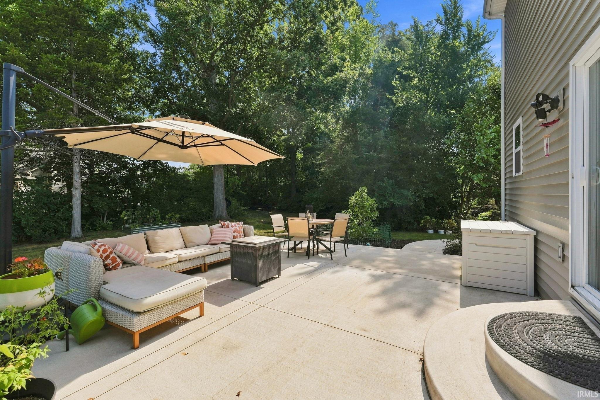 Spacious concrete patio with ample entertaining areas, bordered by mature trees and a manicured lawn