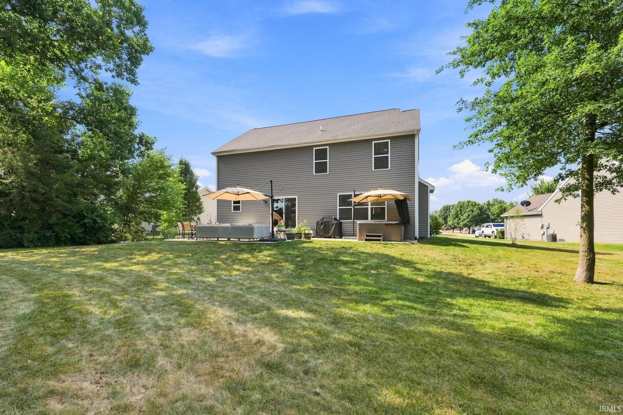 Expansive backyard featuring a stone patio, mature trees, and a two-story exterior with gray siding and multiple windows