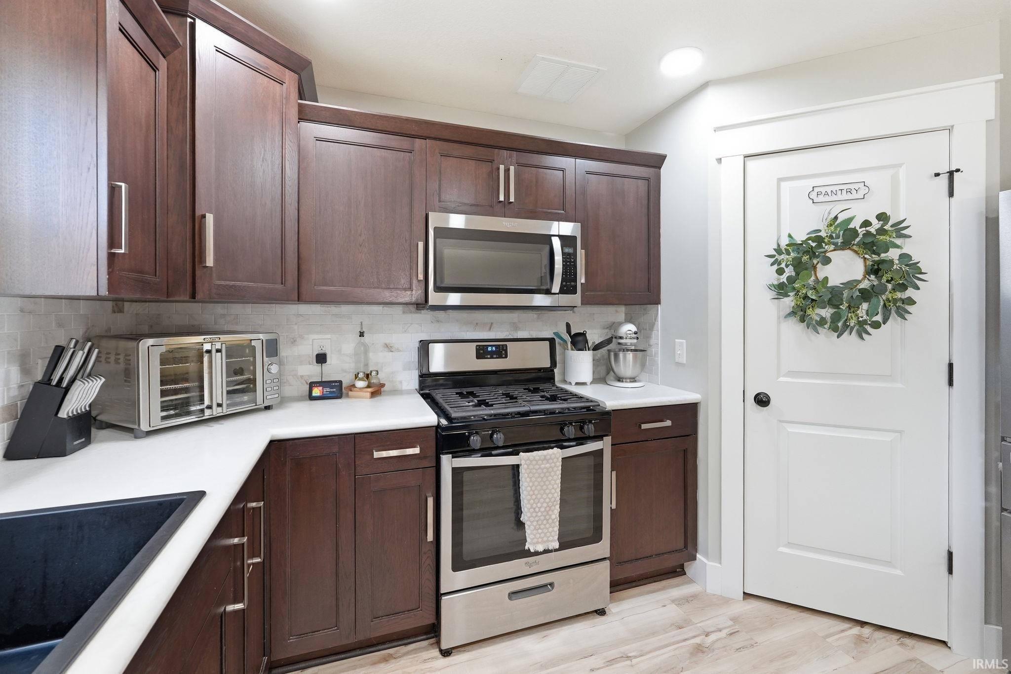Modern kitchen featuring dark wood-finish cabinetry, stainless steel appliances, a white countertop, and a light-toned tile backsplash