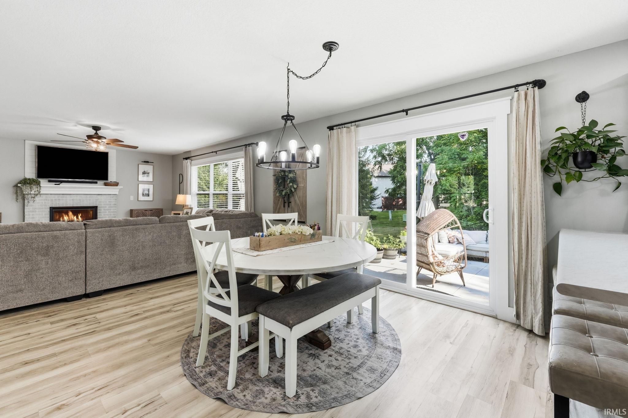 Open-concept living space featuring wood-finish flooring, a white brick fireplace, and a ceiling fan