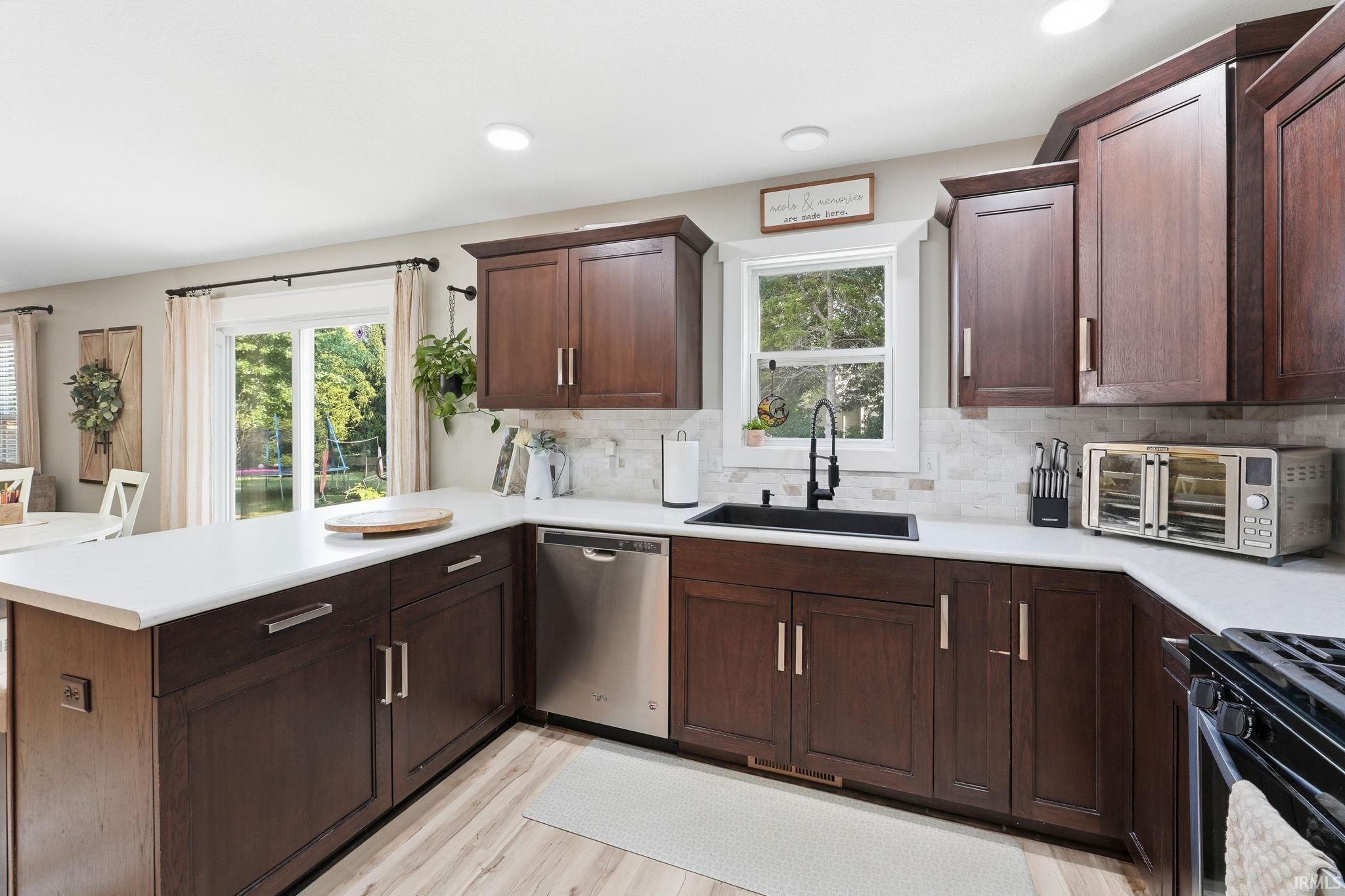Kitchen featuring dark wood-finish cabinetry, white countertops, tile backsplash, and stainless steel appliances