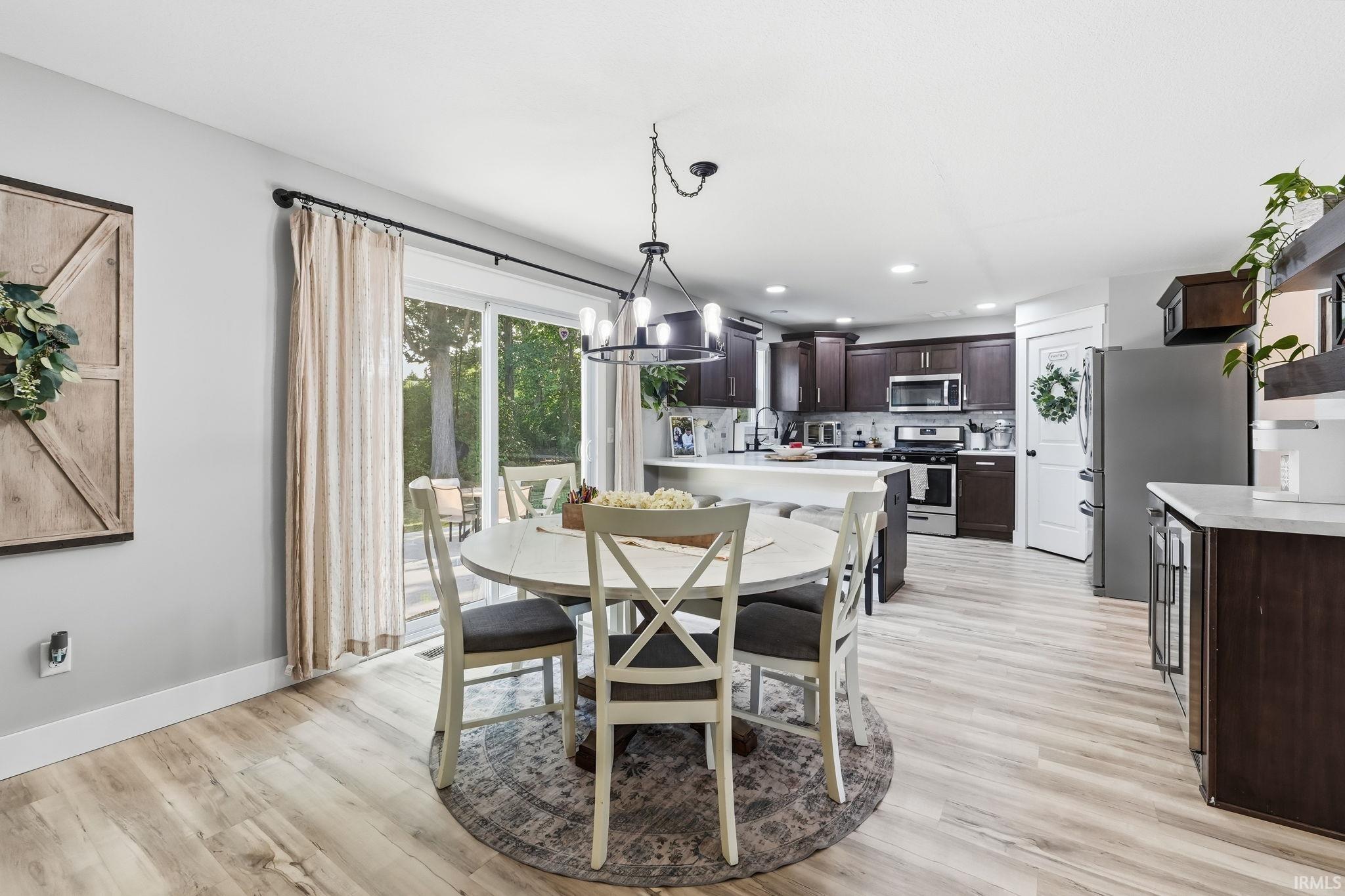 Open concept living space featuring a dining area with a modern chandelier, wood-finish flooring, and a kitchen with dark wood cabinetry