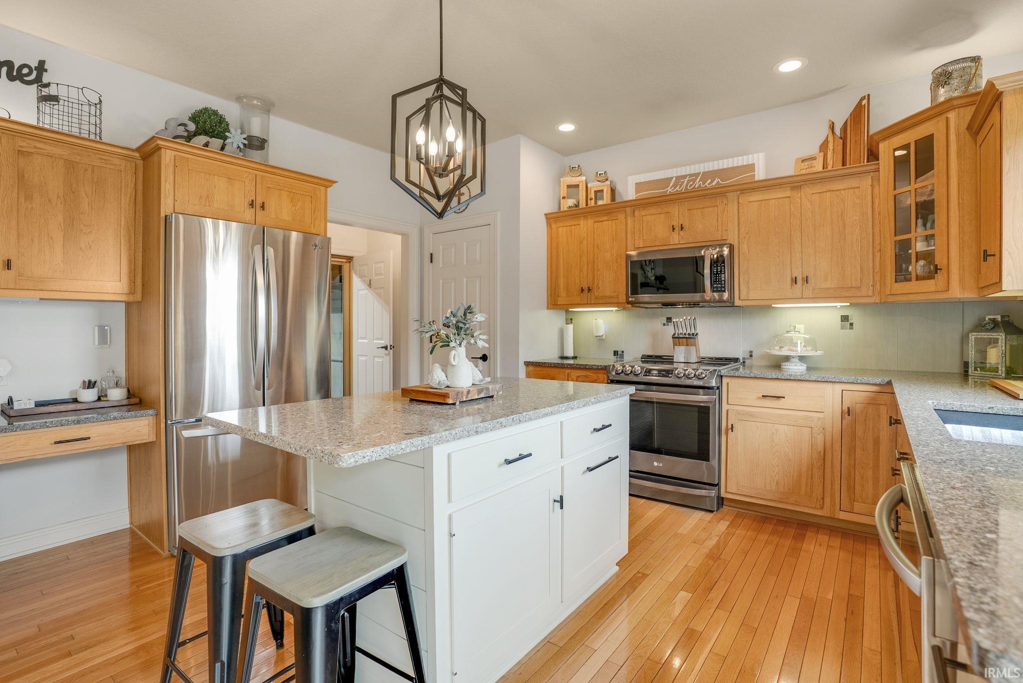 Kitchen featuring wood-finish flooring, light wood cabinetry, stainless steel appliances, and a central island with a light-colored stone countertop
