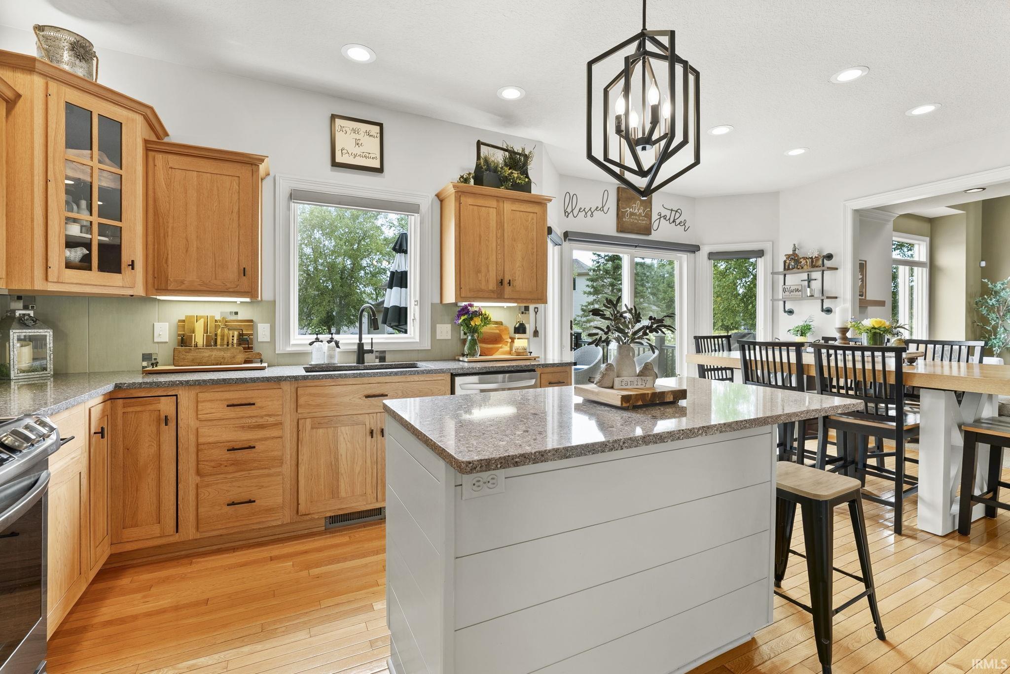 Kitchen featuring wood cabinetry, granite countertops, an island with shiplap detail, wood-finish flooring, and a modern geometric pendant light