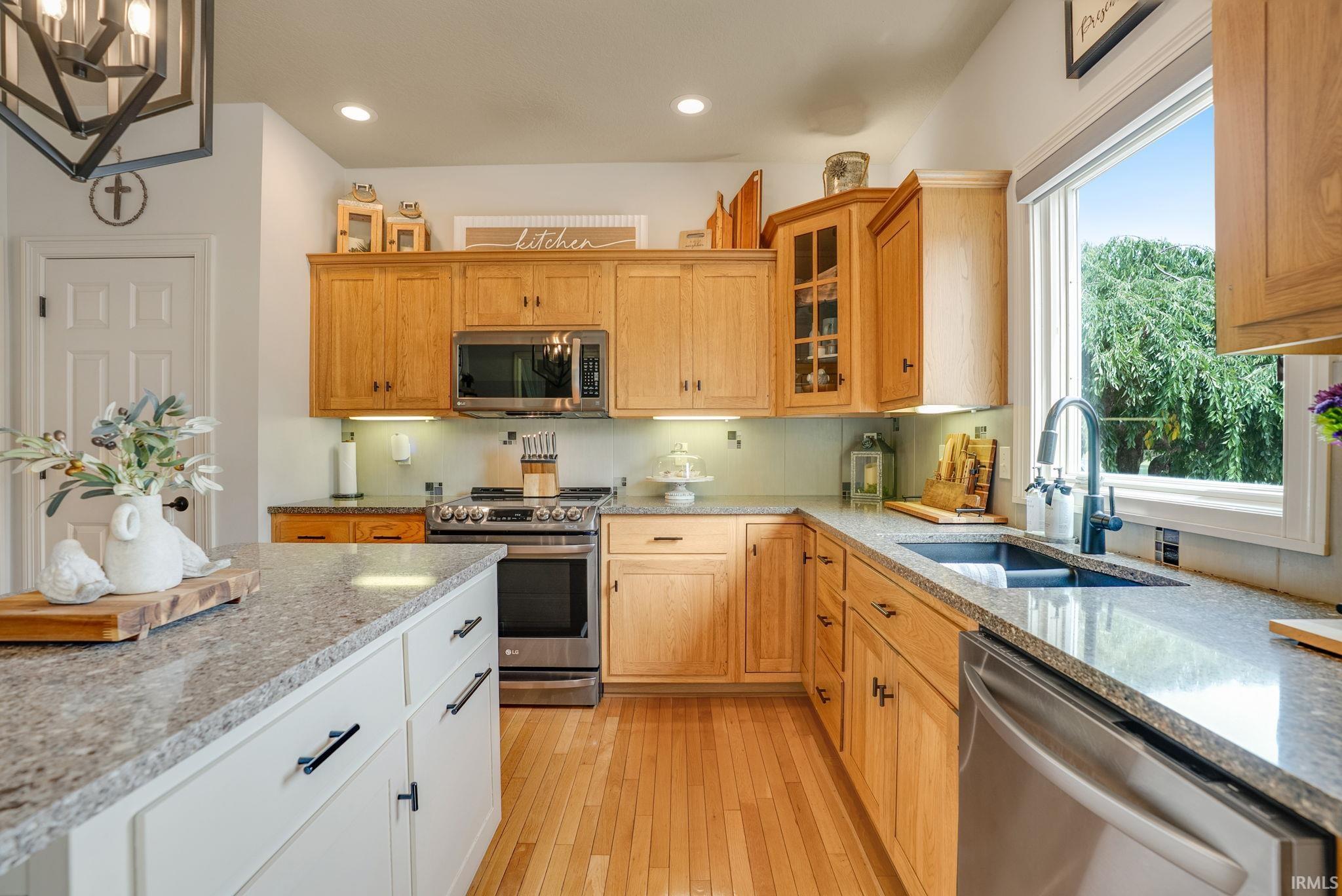 Kitchen featuring wood cabinetry, light granite-finish countertops, stainless steel appliances, a kitchen island with white cabinetry, and wood-finish flooring