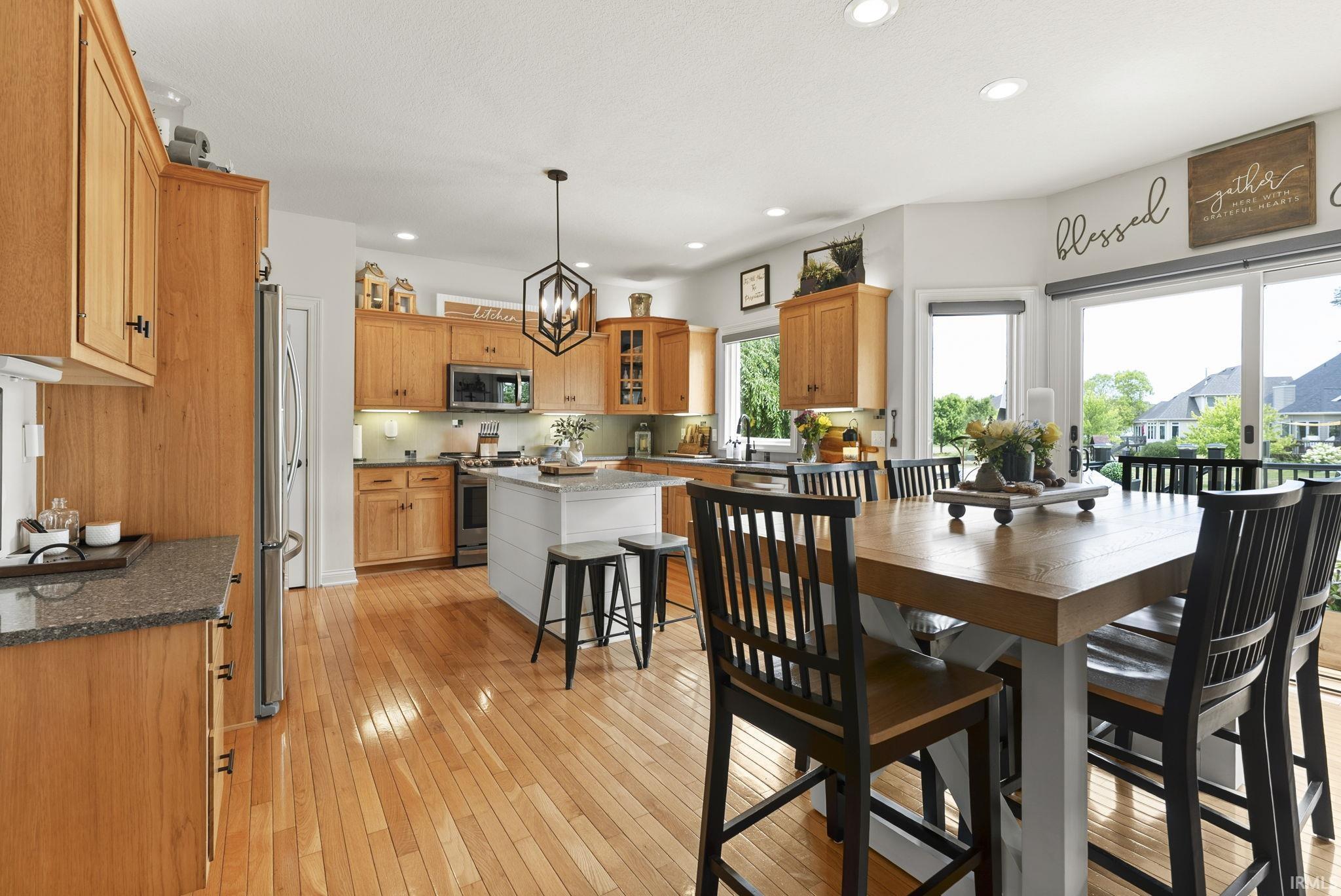 Open-concept kitchen and dining area featuring wood-finish flooring, light wood cabinetry, stone countertops, a central island with shiplap detail, and sliding glass doors to the exterior