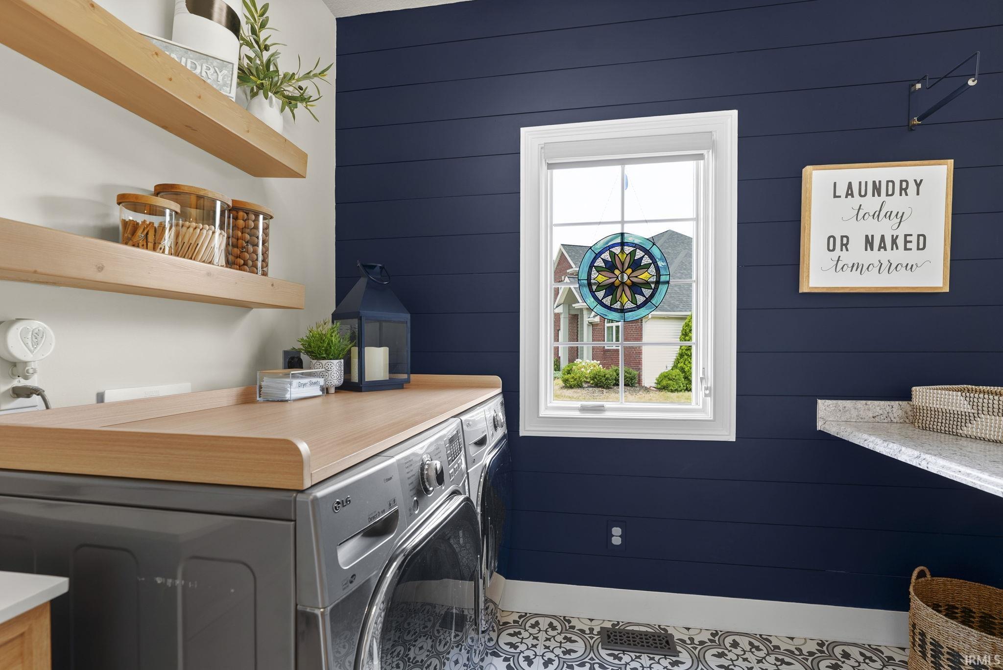 Laundry area featuring shiplap accent wall, wood-finish countertop, floating wood-finish shelving, and patterned floor tile