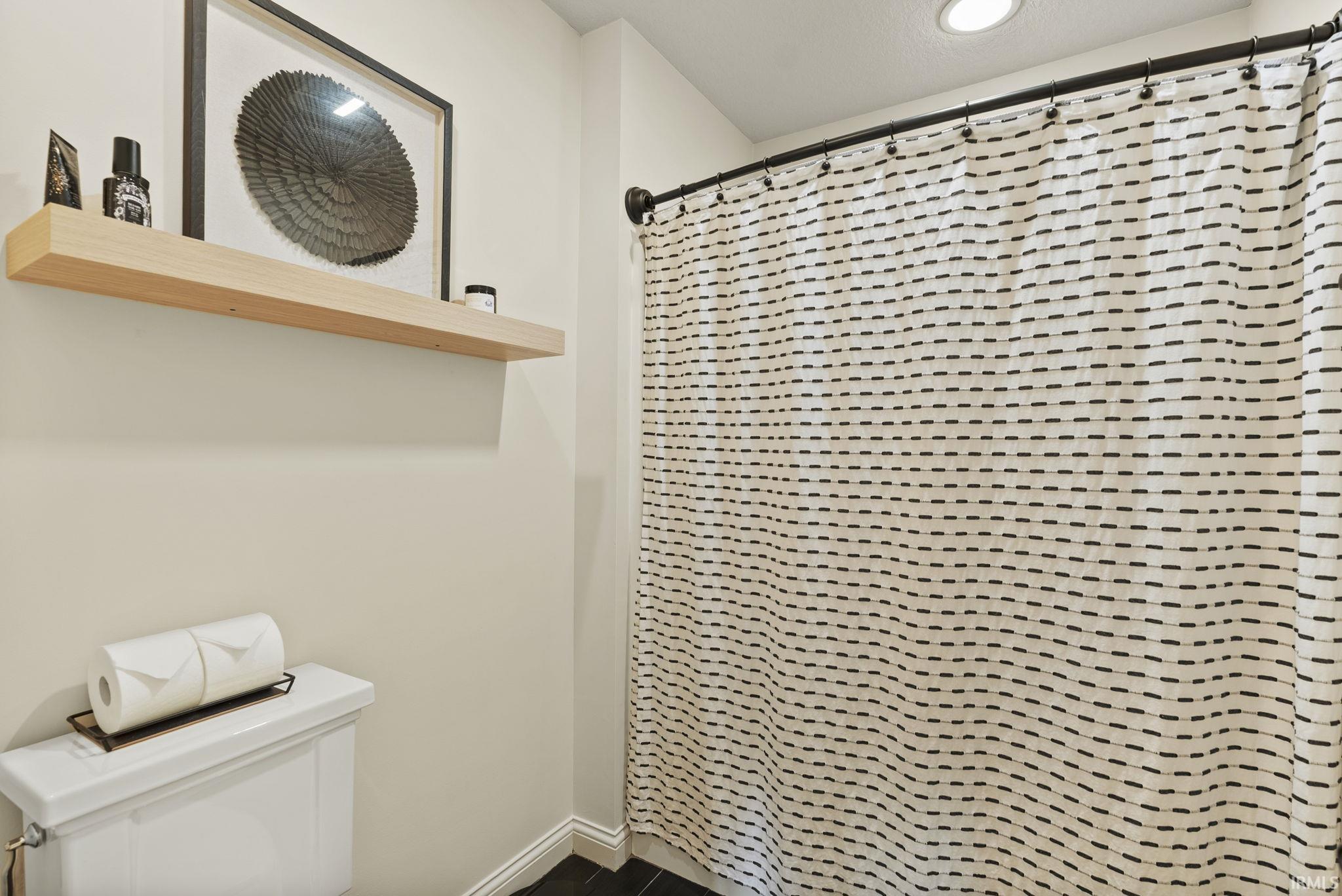 Bathroom featuring a white toilet, recessed lighting, black tile flooring, and a floating wood-finish shelf