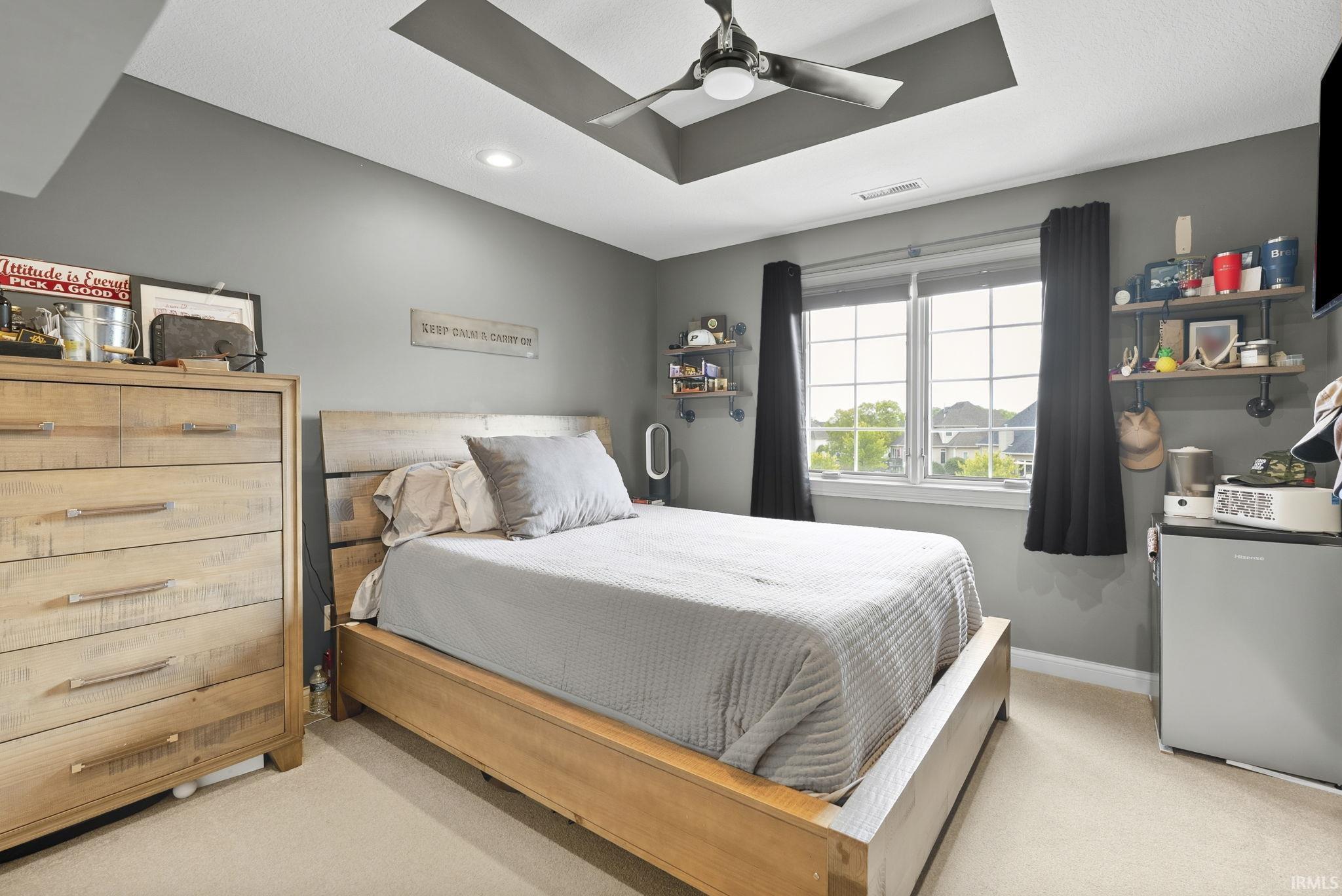 Bedroom featuring a tray ceiling with a ceiling fan, a double window with grid panes, and neutral carpeting