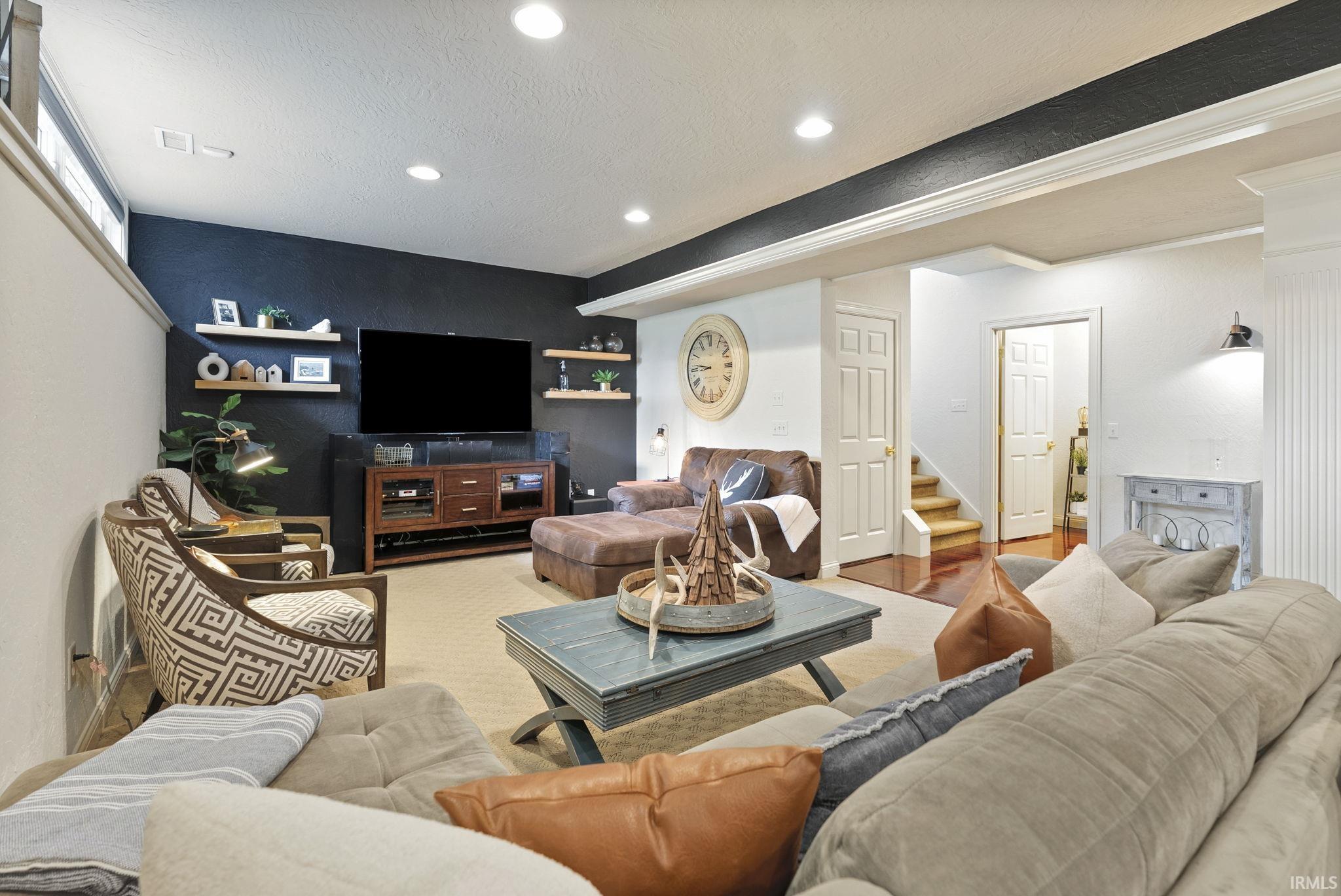 Spacious entertainment room featuring recessed lighting, a dark accent wall, and wood-finish floating shelves
