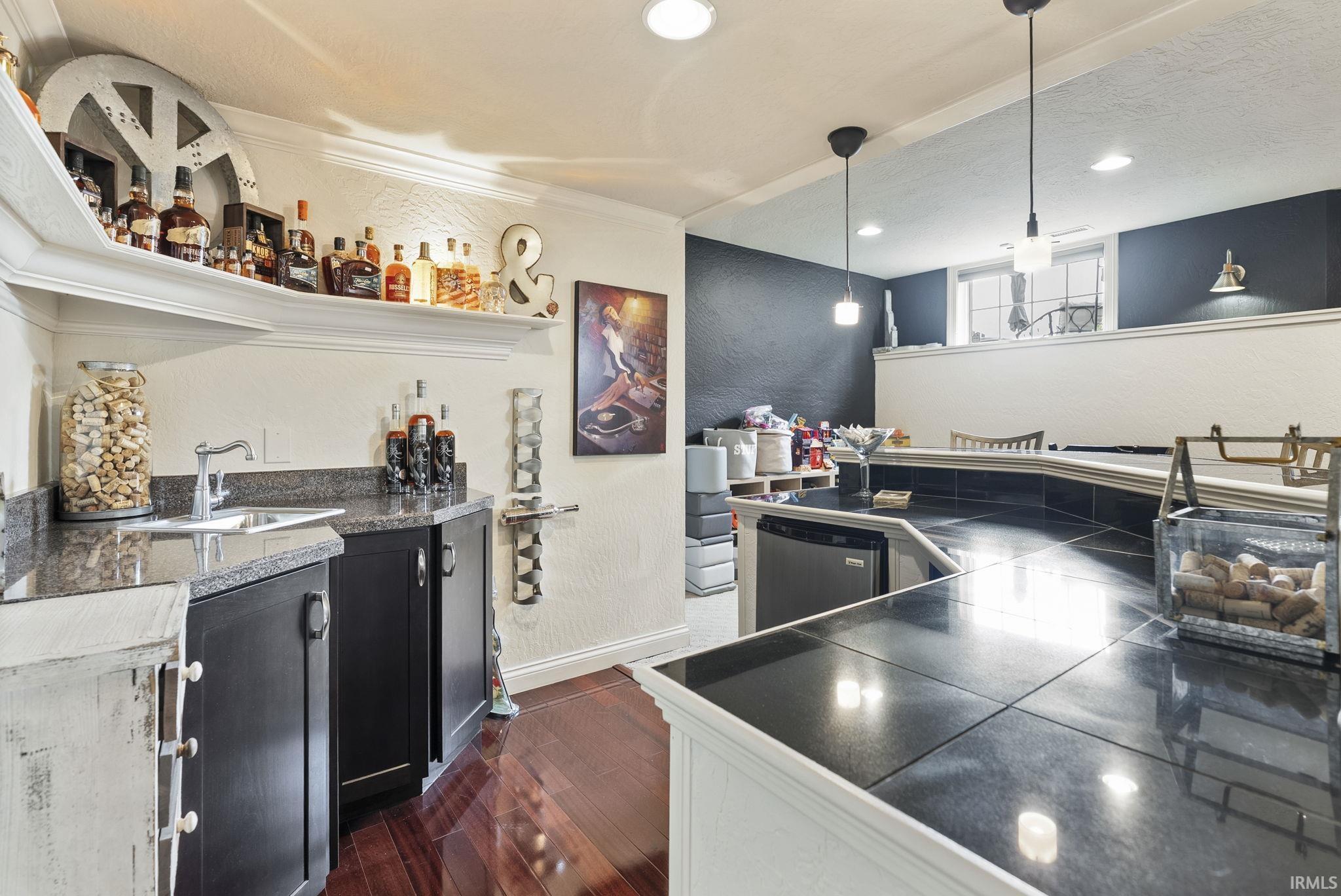 Wet bar featuring a dark granite countertop, a stainless steel under-counter refrigerator, built-in cabinetry, and wood-finish flooring