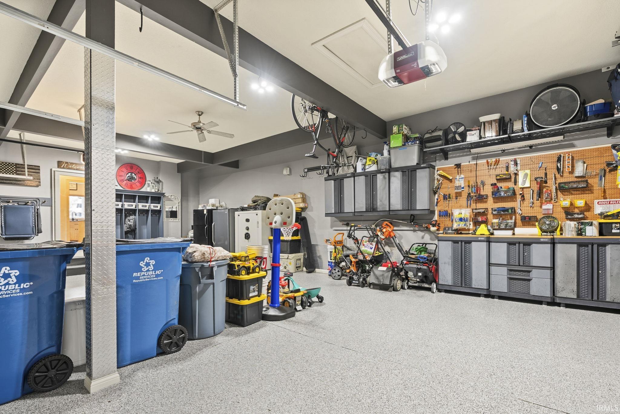 Spacious garage featuring an epoxy floor, extensive built-in cabinetry, a pegboard organization system, overhead shelving, and an exposed beam ceiling