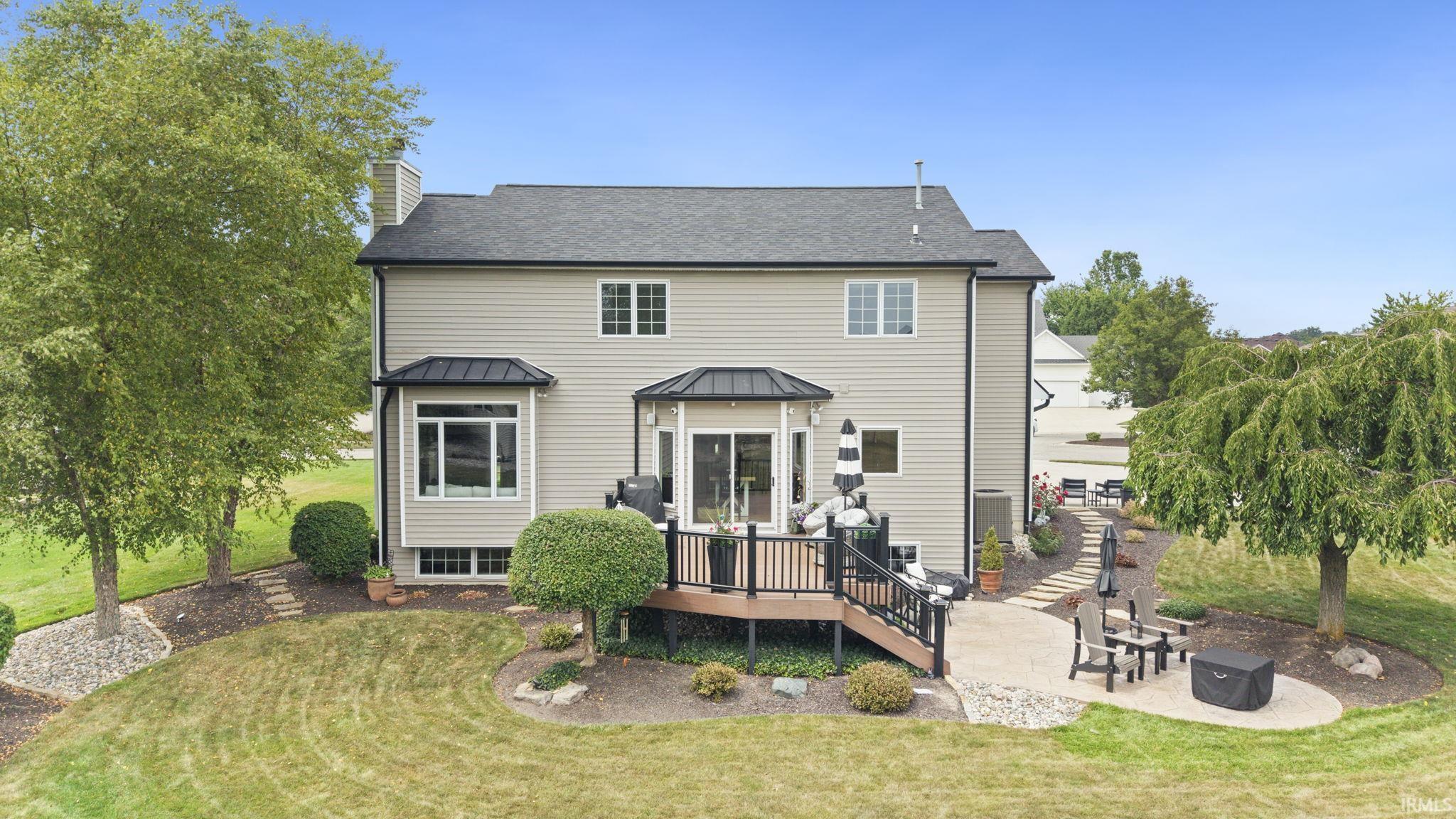 Charming Colonial-style residence showcasing a manicured lawn with mature landscaping, curved brick paver patio, and multi-level composite deck