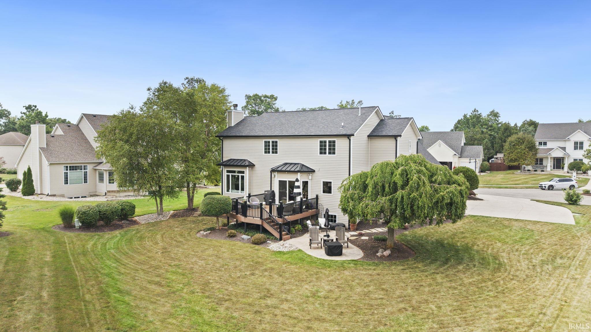 Expansive rear yard featuring a multi-level wood-finish deck with built-in railing, a circular paver patio, and mature trees